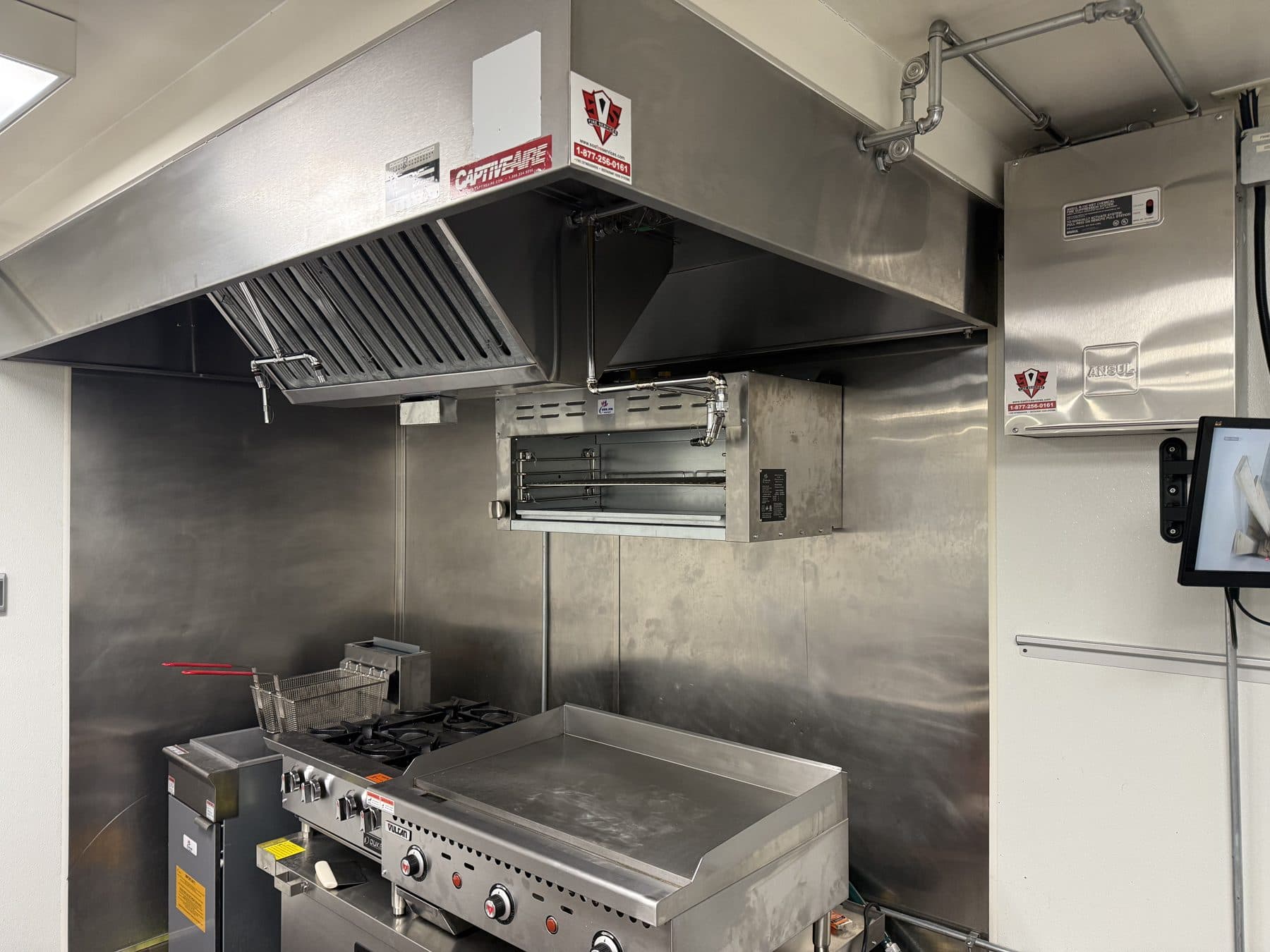 Restaurant cook line under a hood with ANSUL R-102 nozzle piping and the system cabinet mounted on the wall