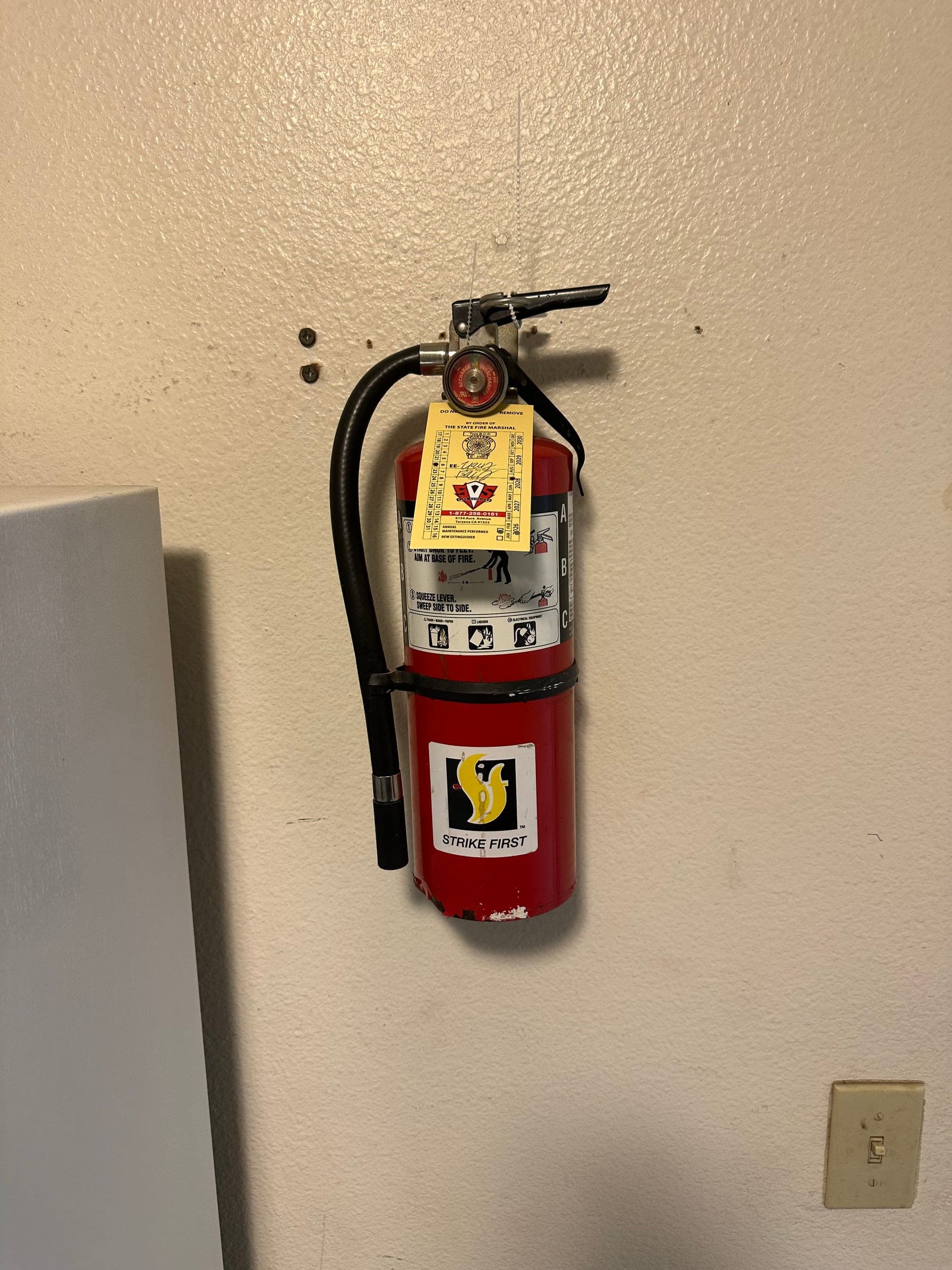 Strike First 5 lb ABC extinguisher hung on a wall bracket with a yellow service tag