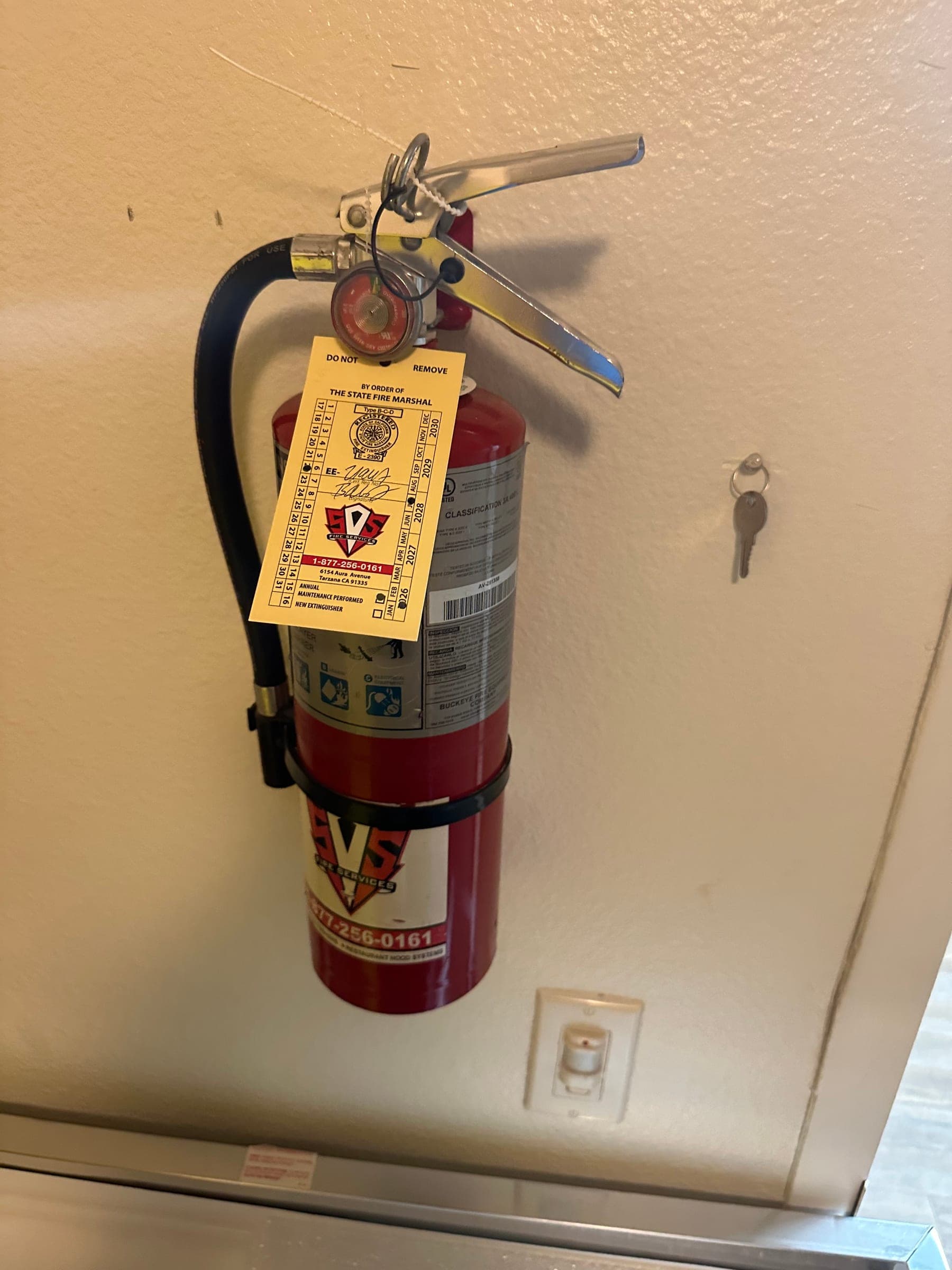 Buckeye 5 lb ABC extinguisher mounted on a bracket with a fresh State Fire Marshal tag