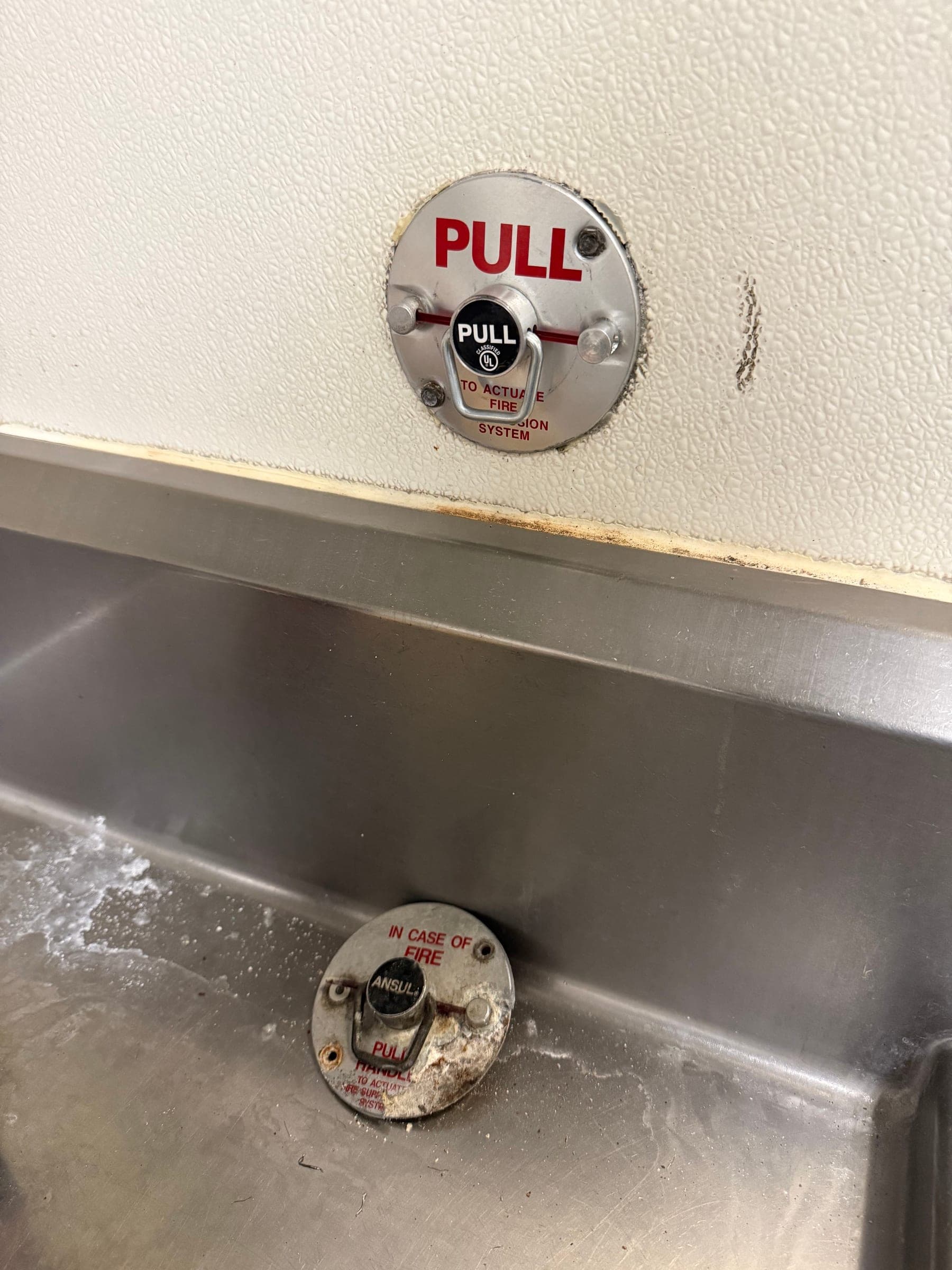 New pull station mounted on the wall with the old corroded one set down in the sink below