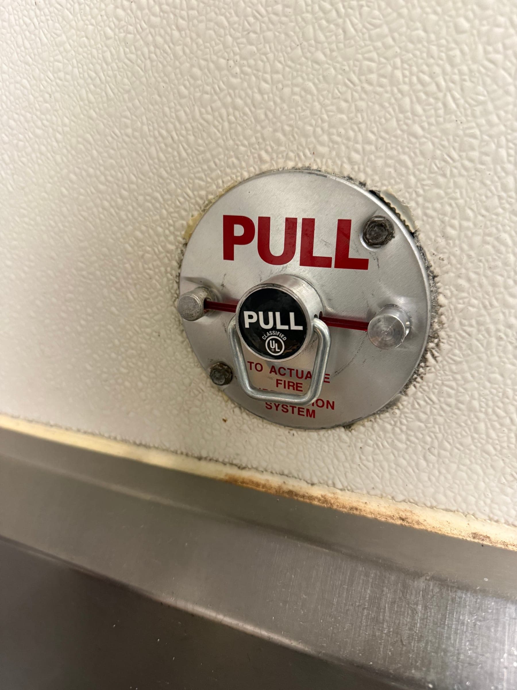 New manual pull station with a red PULL faceplate and ring handle, sealed to the kitchen wall