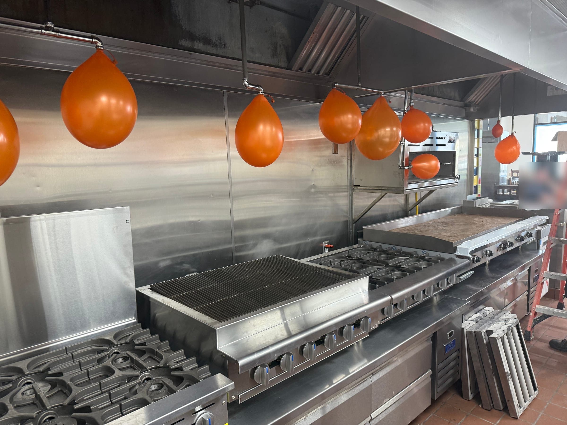 Orange test balloons fitted to every Ansul R-102 nozzle above a charbroiler, range and griddle