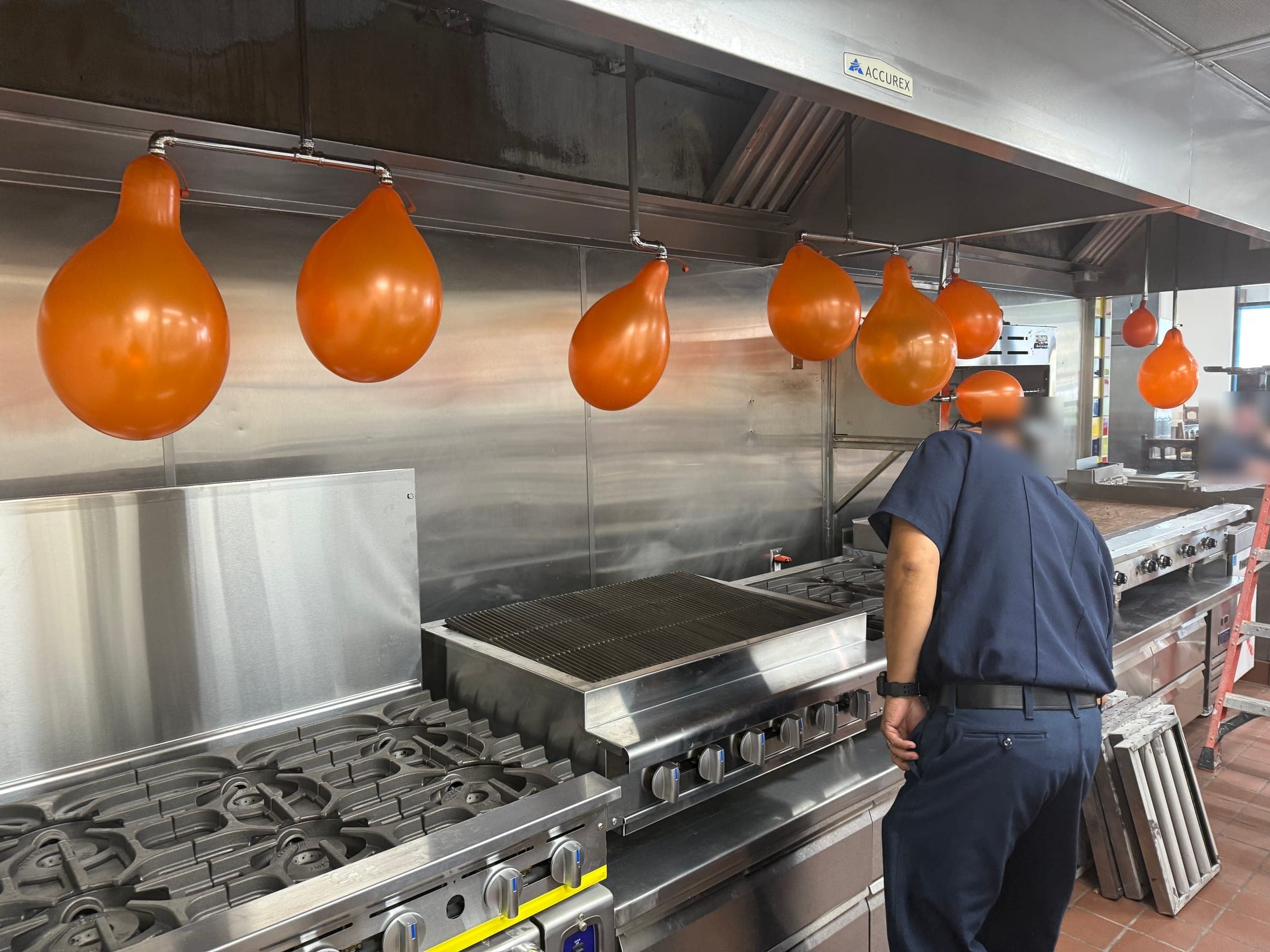 Person in a dark uniform reviews the ballooned Ansul R-102 nozzles over the cooking line