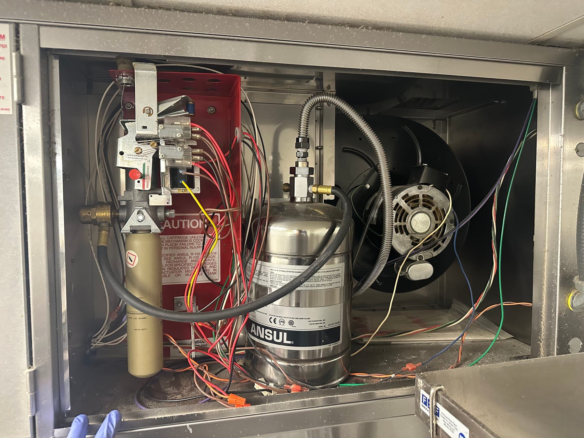 Compact Ansul cylinder, release mechanism and blower fan inside the cabinet of a ventless hood, wiring exposed for testing