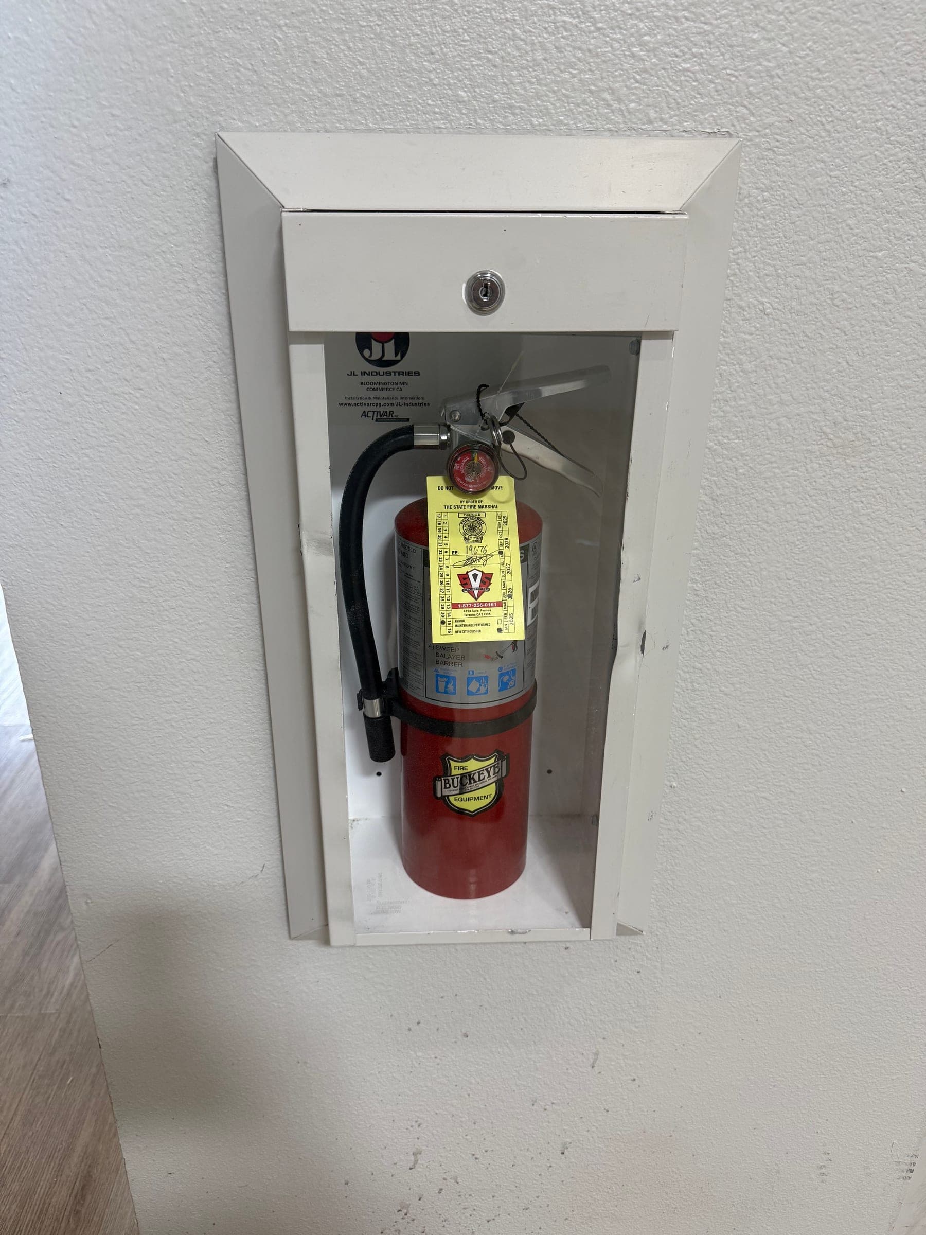 Semi-recessed extinguisher cabinet holding a tagged 5 lb ABC extinguisher in a corridor