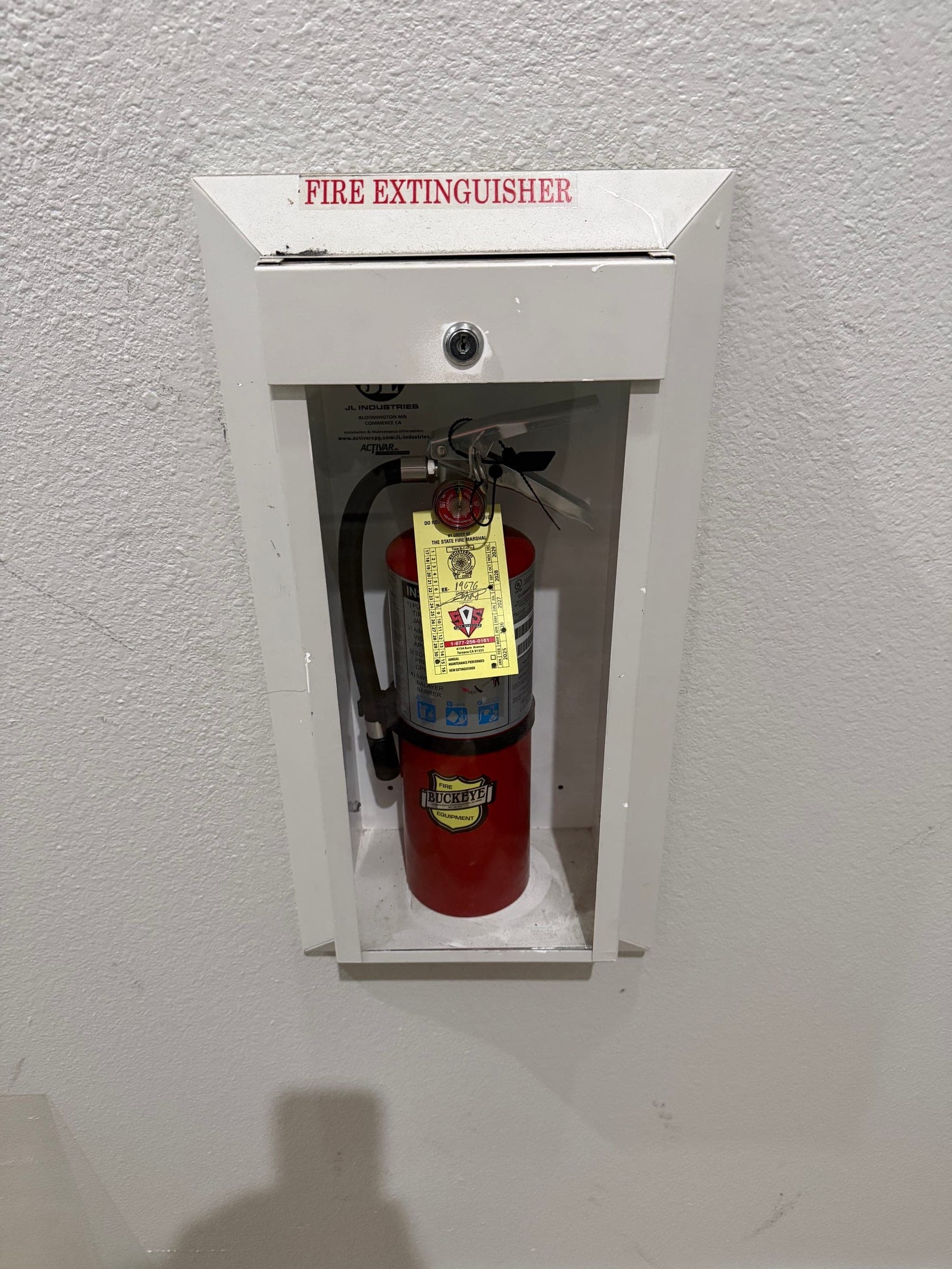 Labeled extinguisher cabinet with a locked door and a tagged 5 lb ABC extinguisher inside