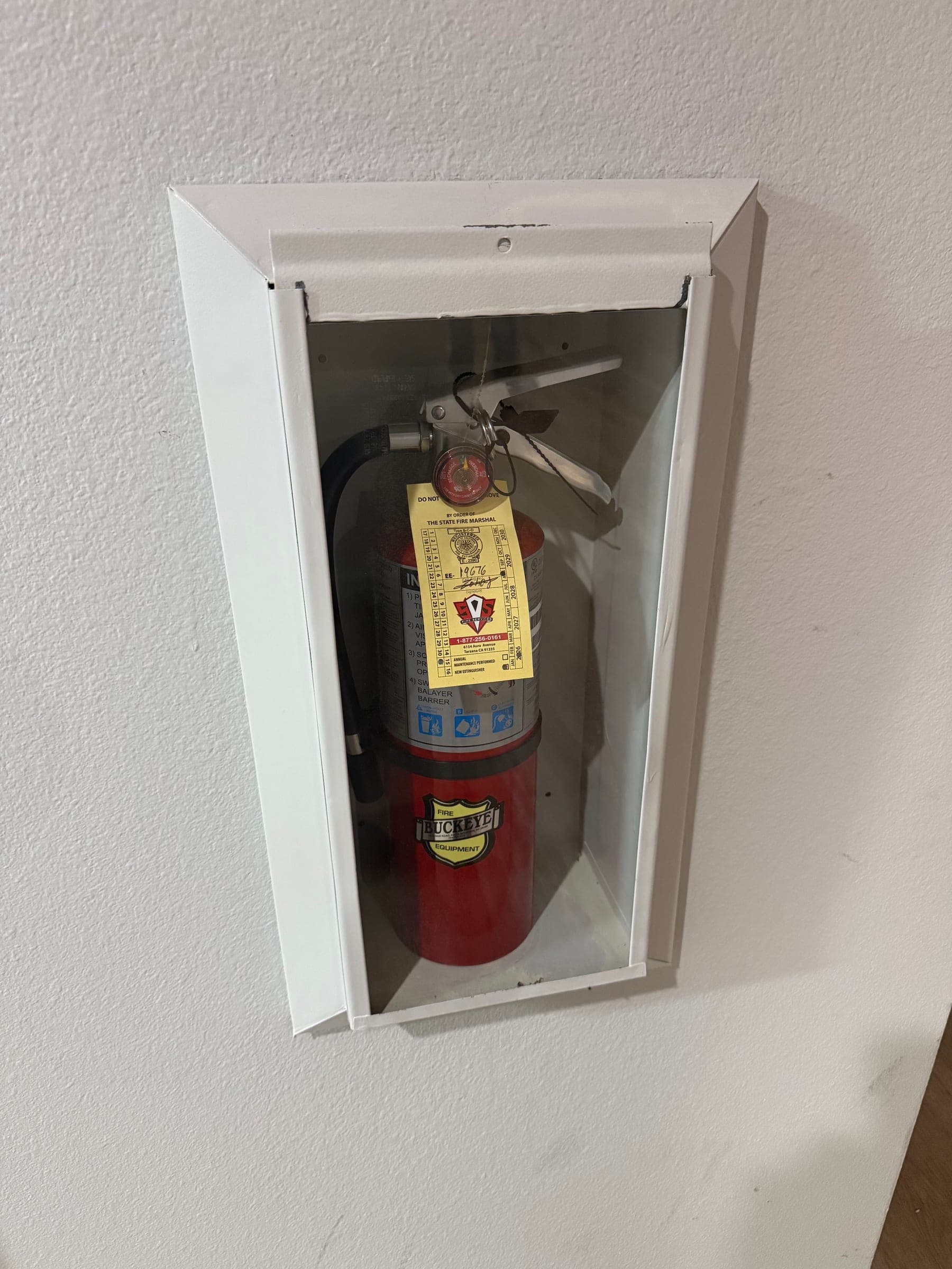 Recessed cabinet with a tagged 5 lb ABC extinguisher, gauge and pull pin visible