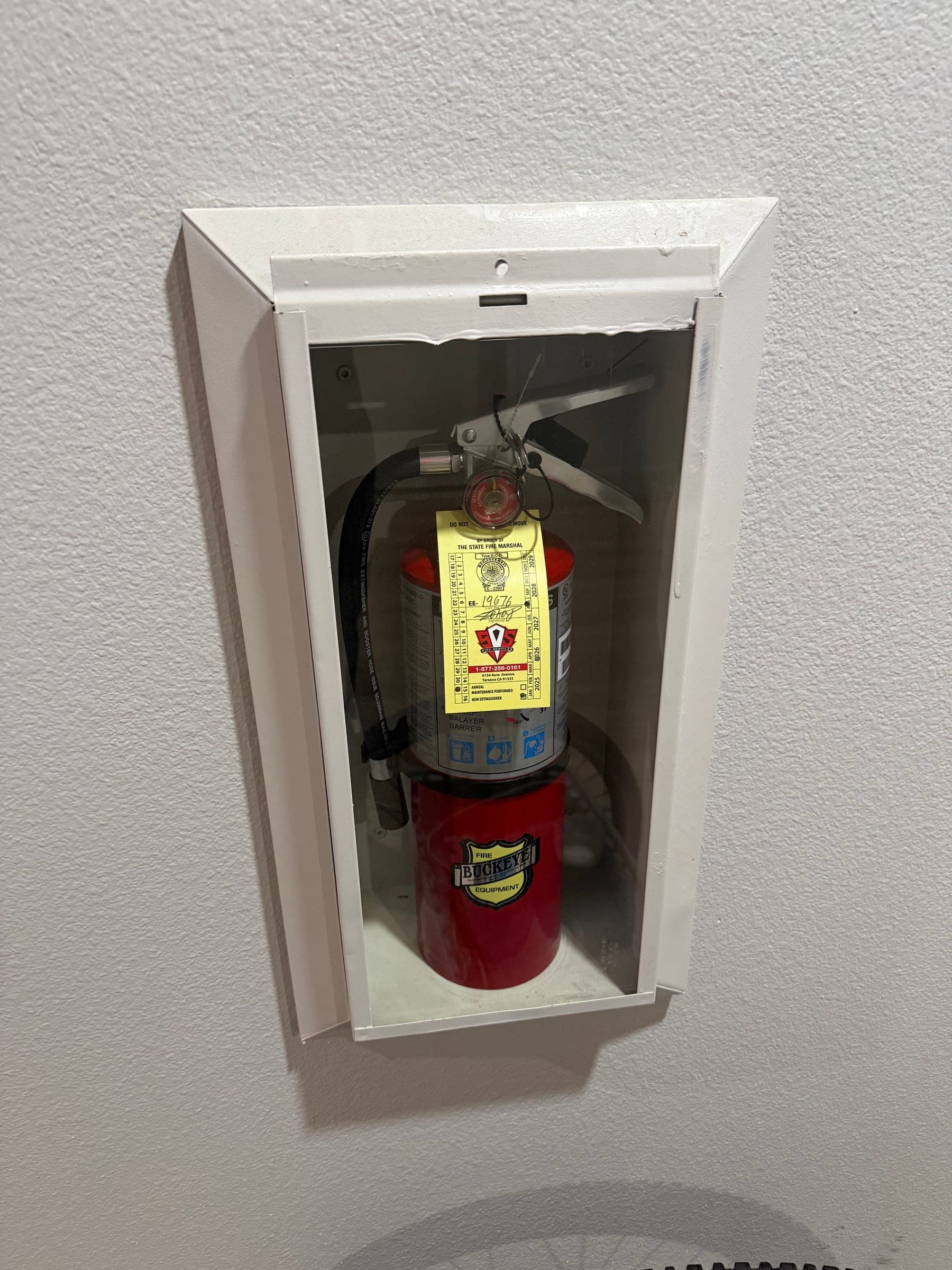Recessed cabinet in a stairwell wall holding a tagged ABC extinguisher