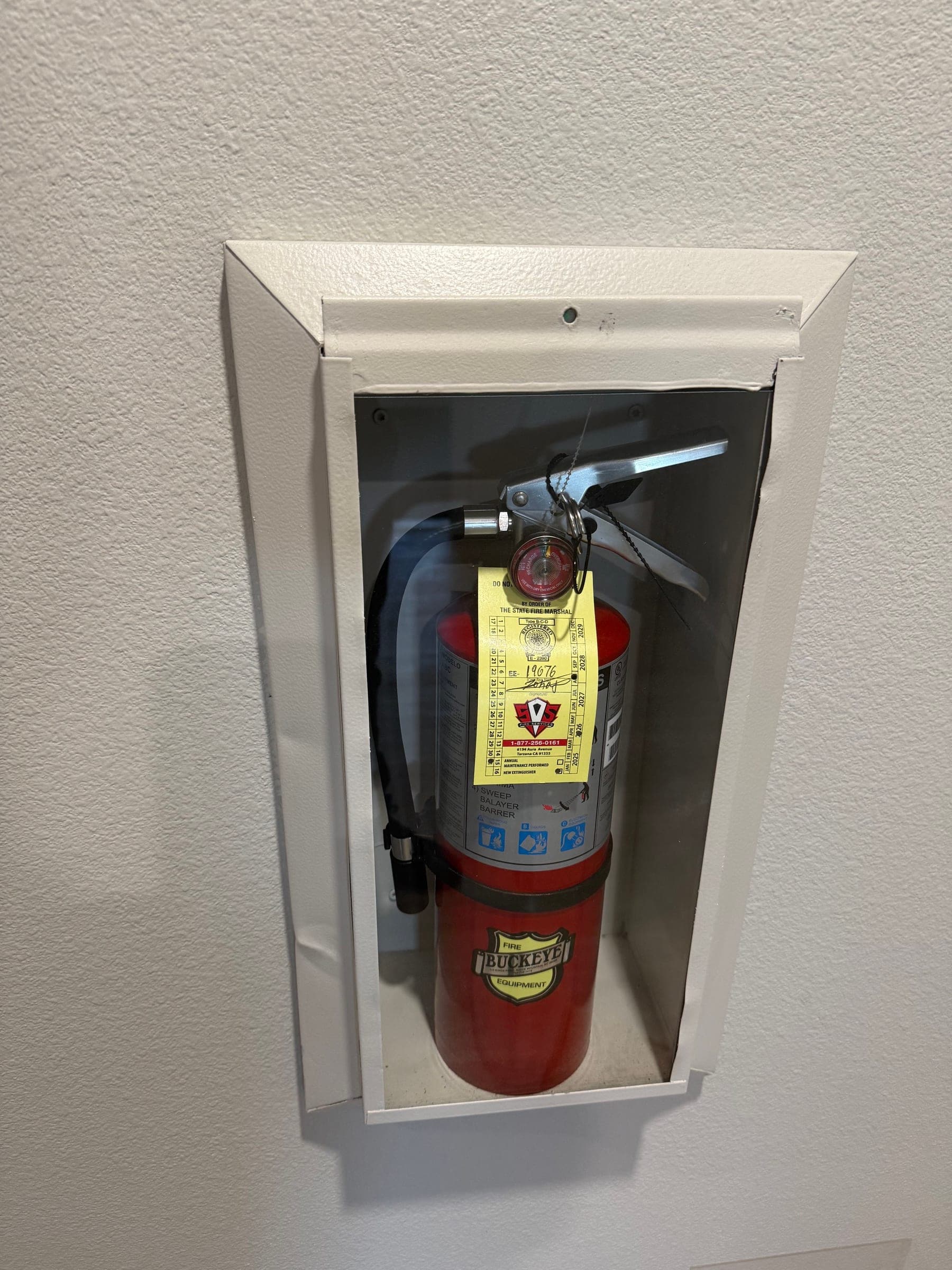 Recessed extinguisher cabinet on a textured wall with a newly tagged ABC extinguisher