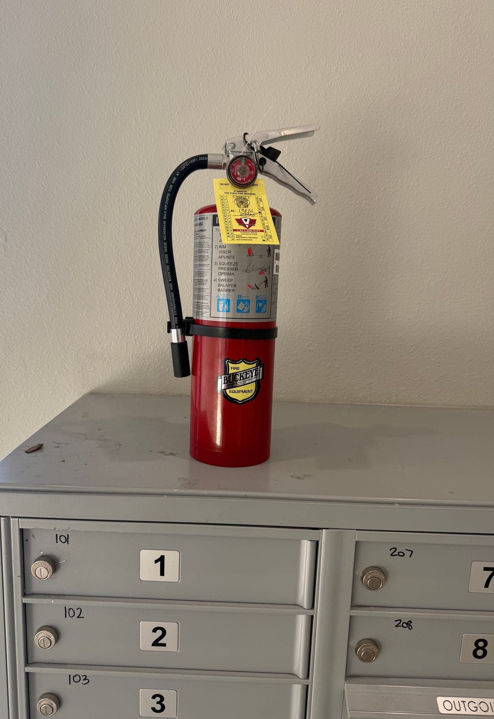Tagged 5 lb ABC extinguisher standing on top of a cluster mailbox unit
