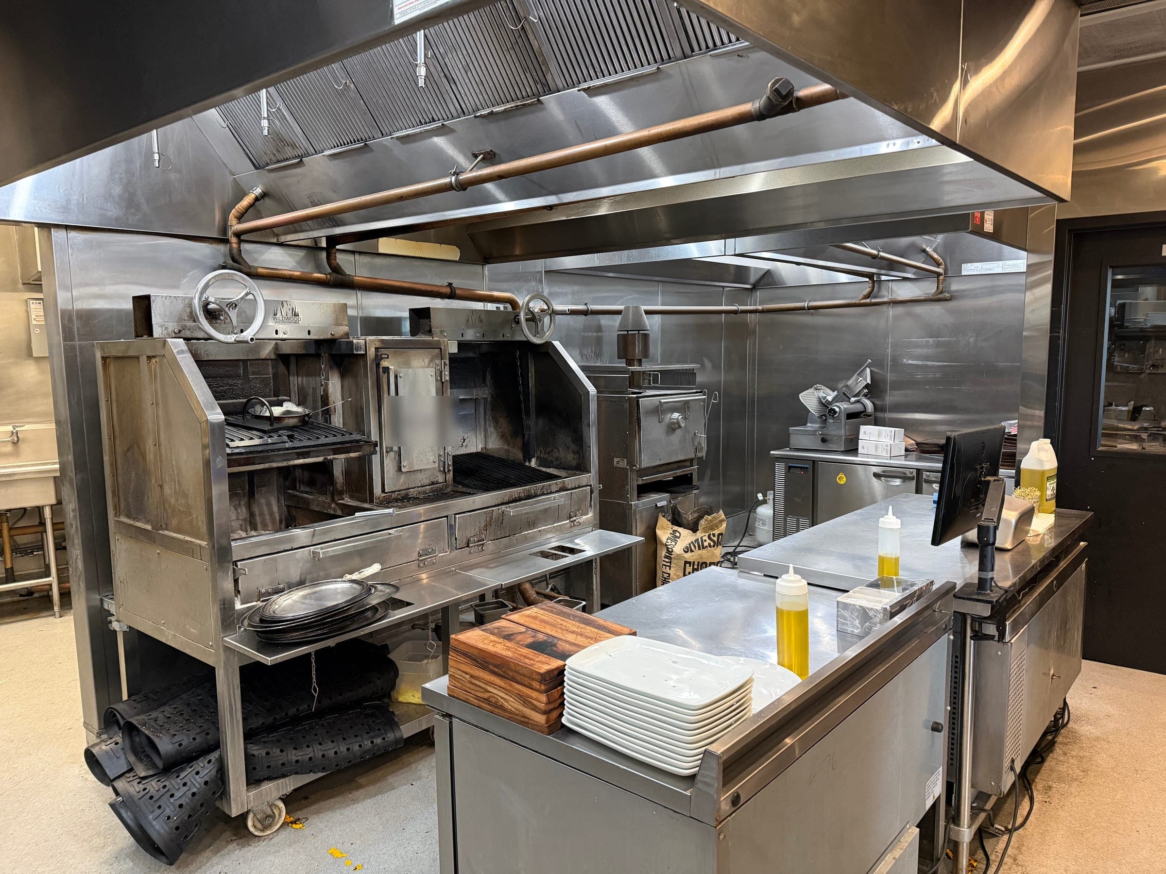 Wood-fired grill line under the hood with suppression piping and nozzles, buckets removed