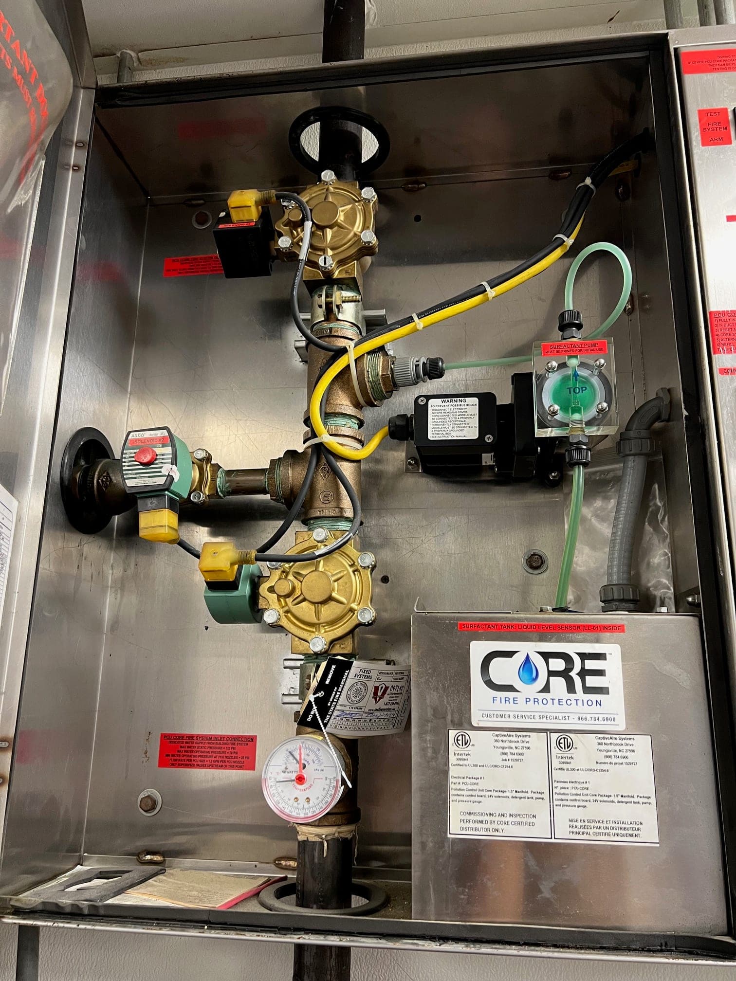 Open CaptiveAire CORE cabinet showing the water manifold, solenoid valves, pressure gauge and surfactant tank