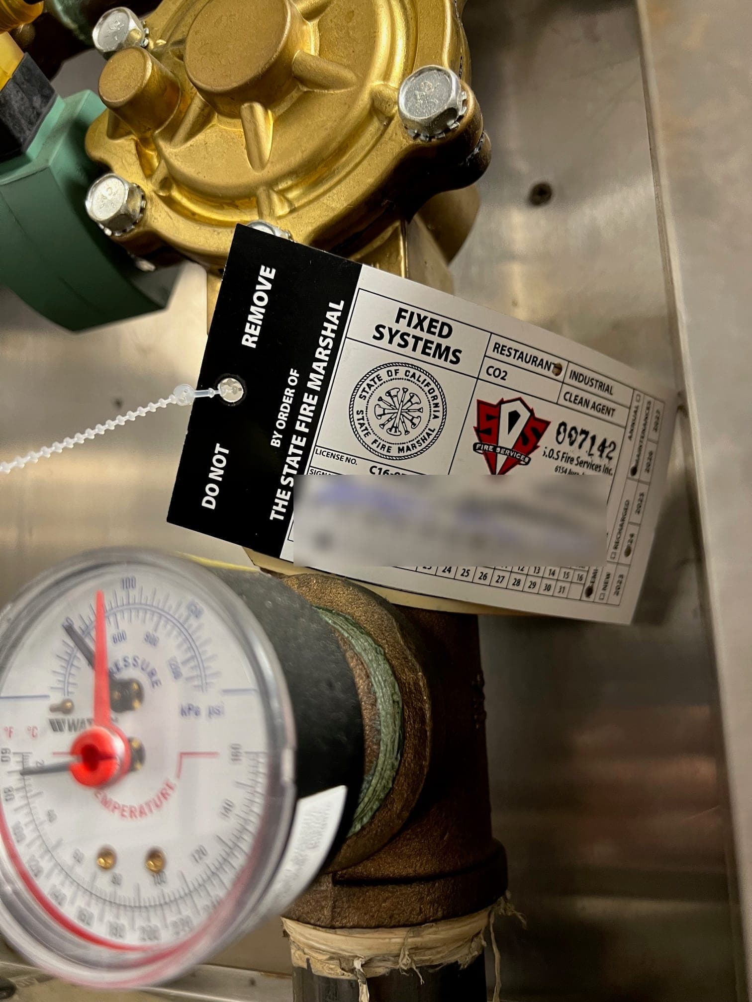 State Fire Marshal fixed-systems tag hung on the CORE valve above the pressure and temperature gauge