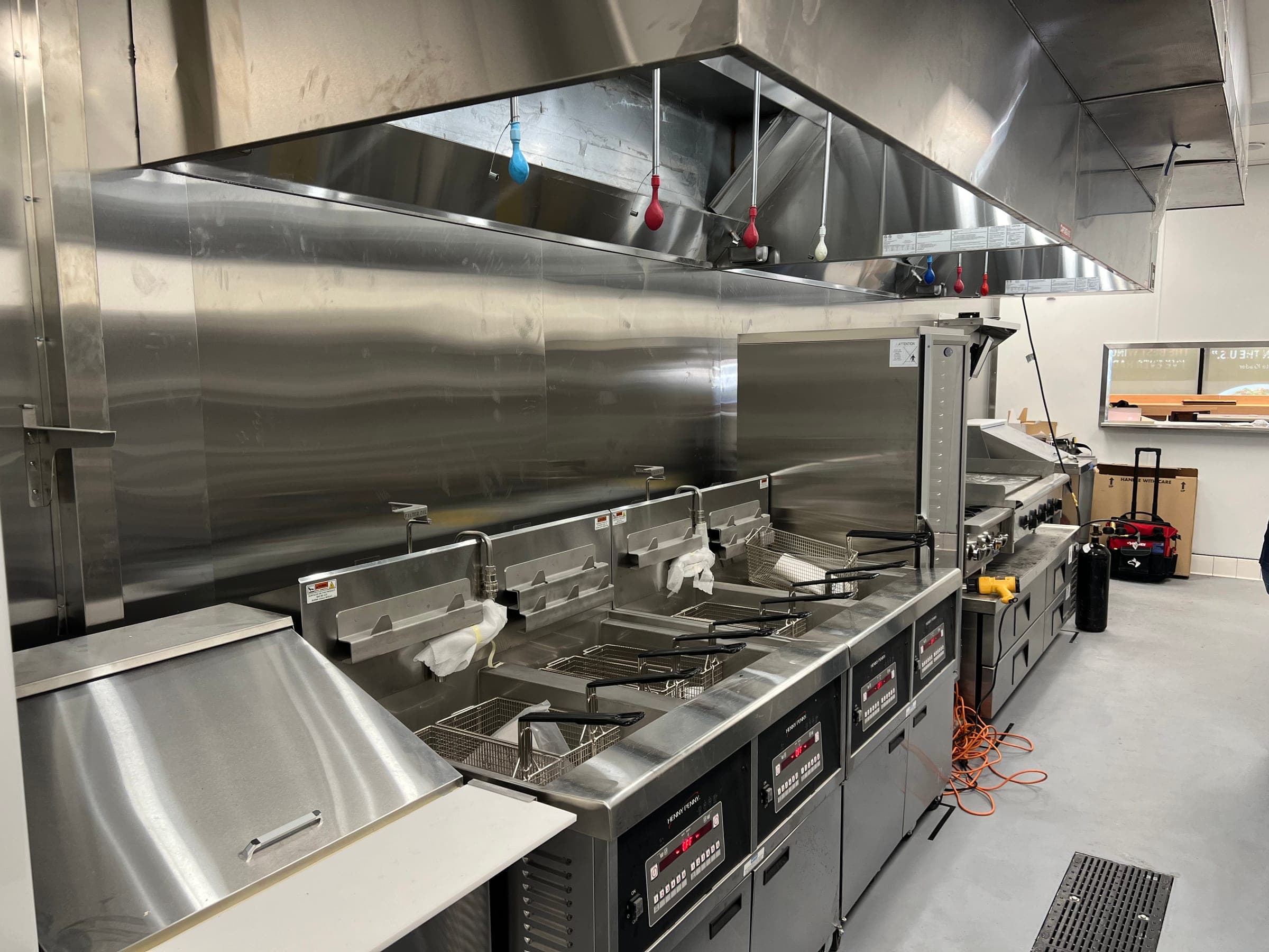Wide view of the fryer line under the hood with balloons fitted on every suppression nozzle