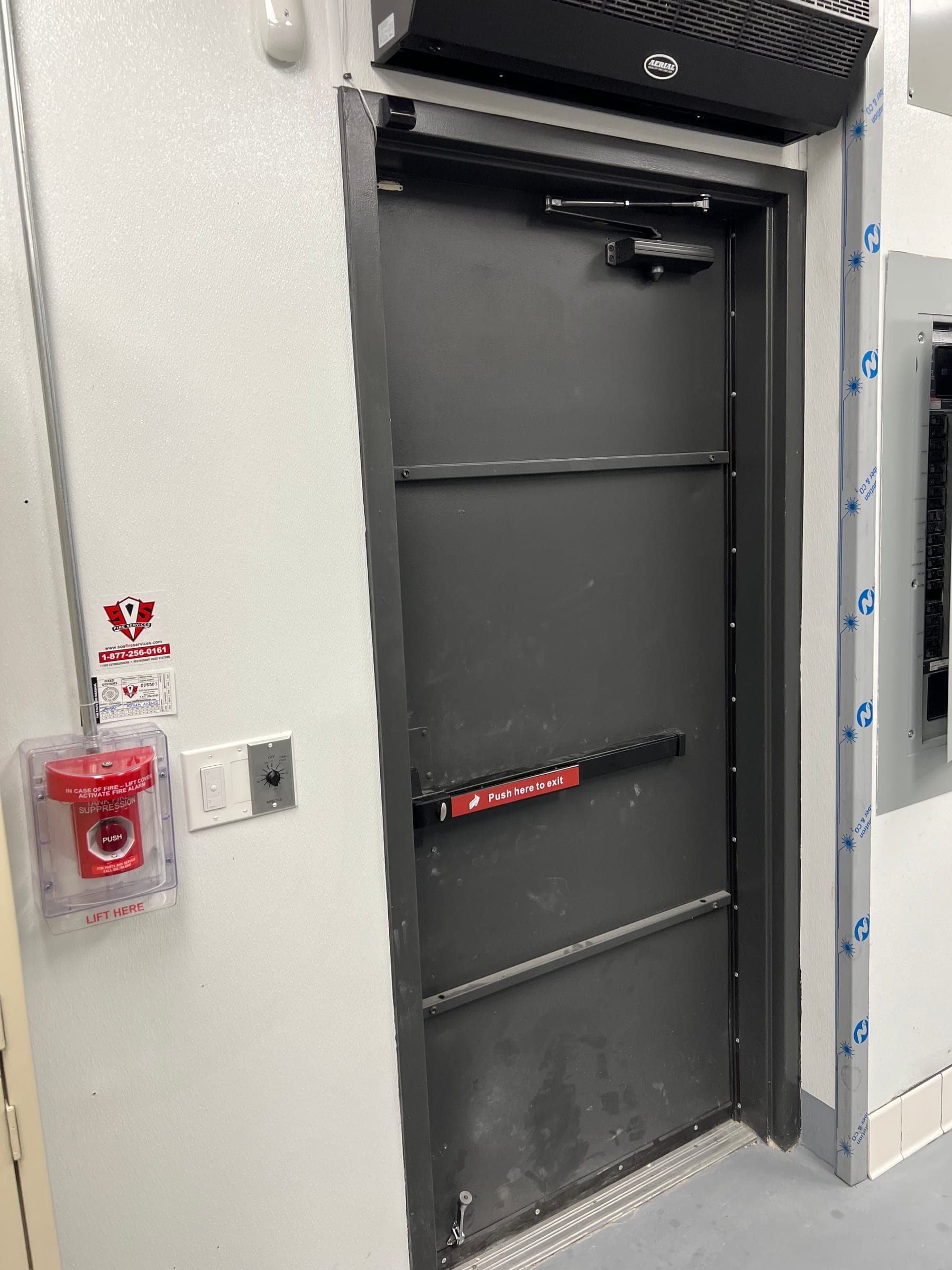Tank fire suppression manual push station with service tag mounted by the kitchen exit door