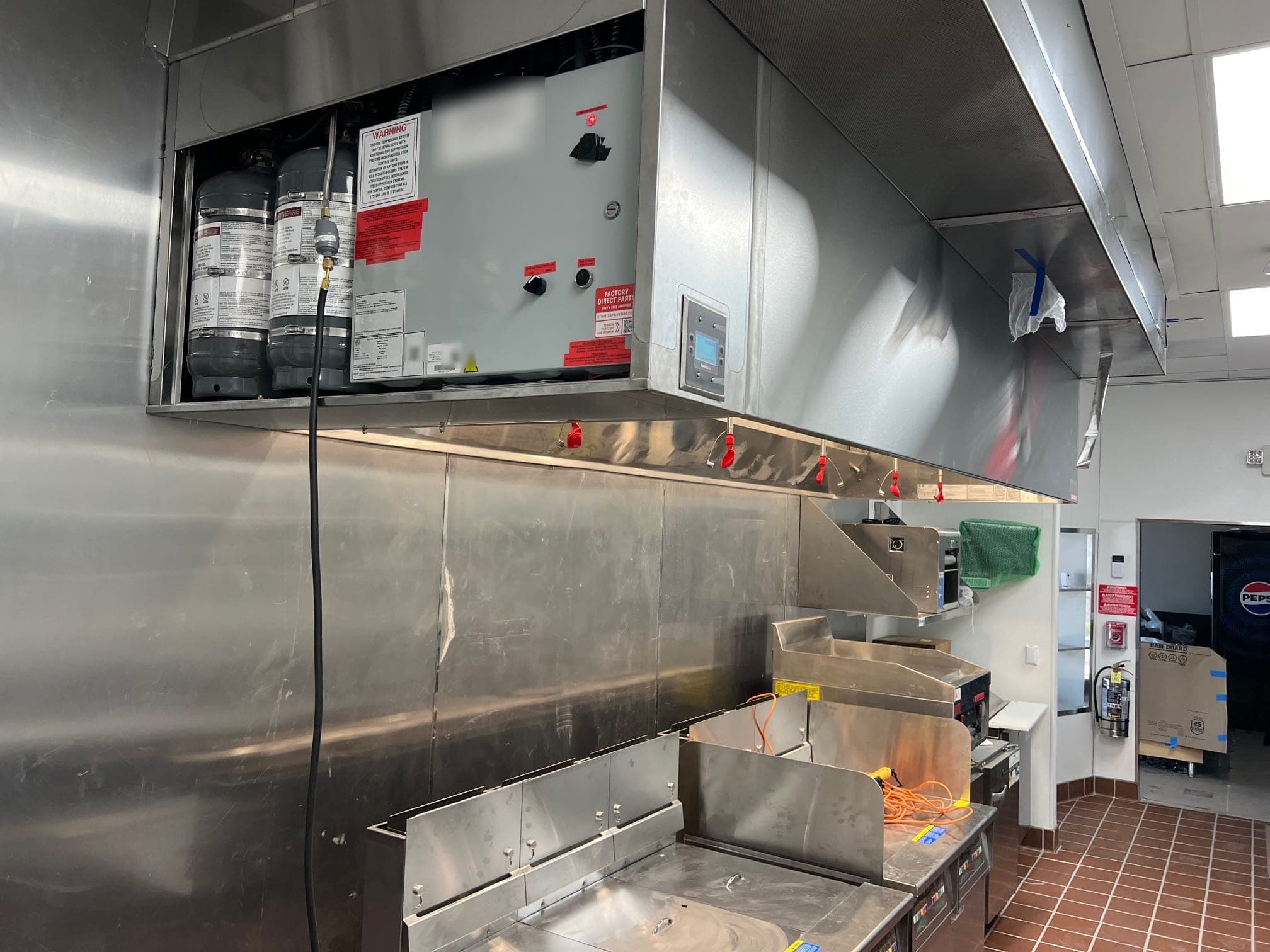 CaptiveAire hood cabinet with two tank cylinders and control panel above a new fryer line