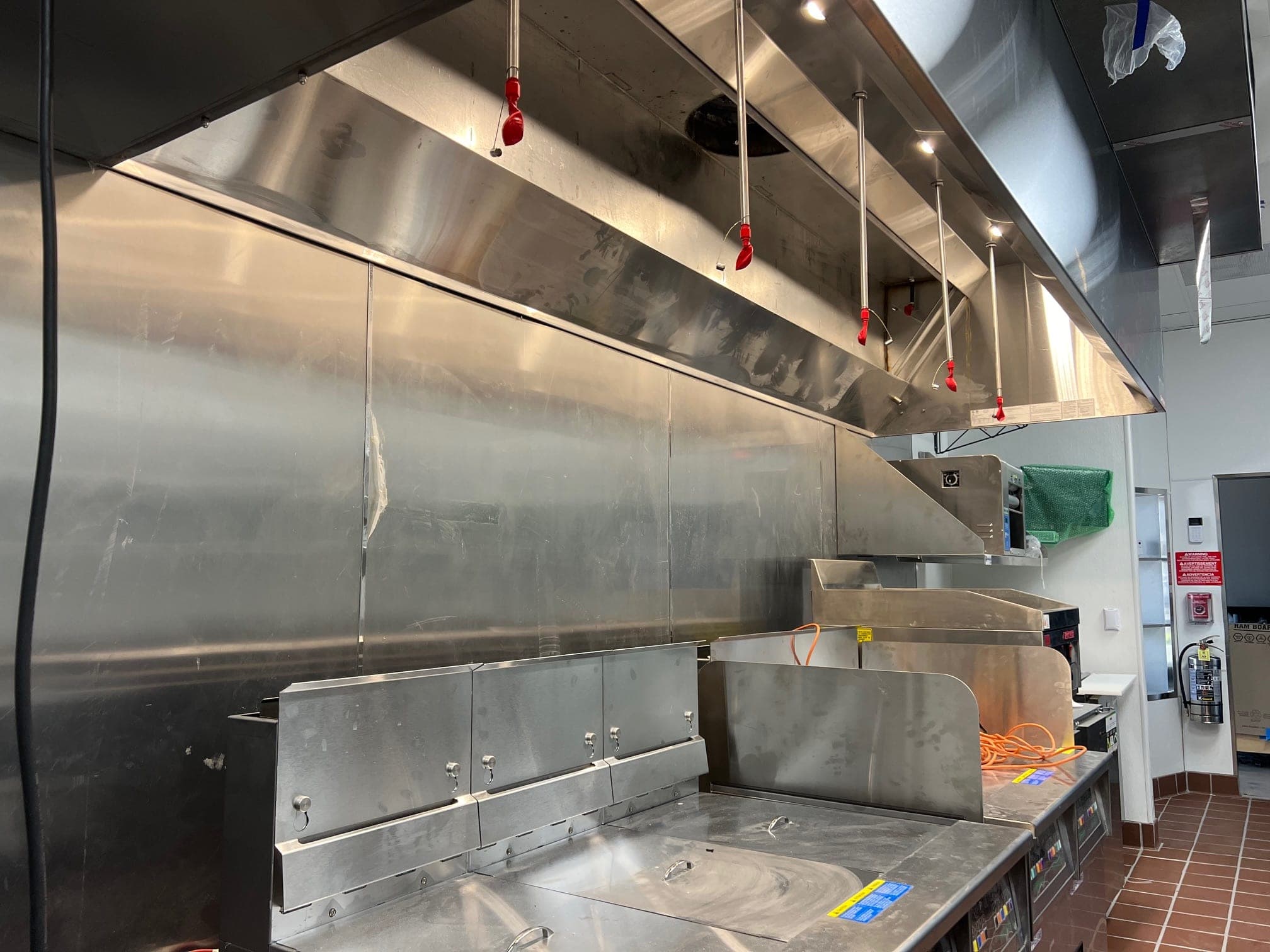 Suppression nozzles with red covers spaced along the hood above fryers