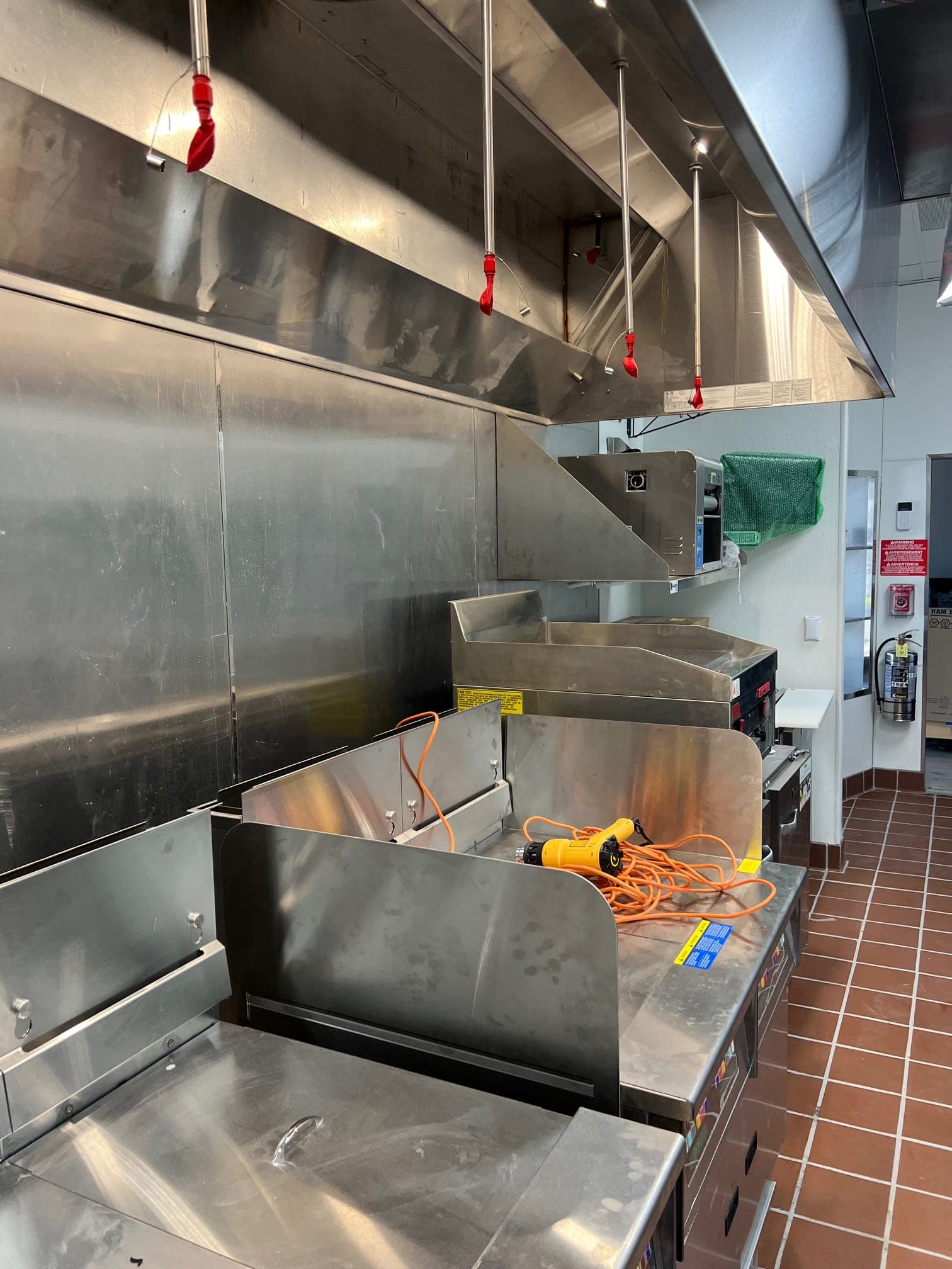 Hood nozzles with red covers over fryers, with a Class K extinguisher mounted by the doorway
