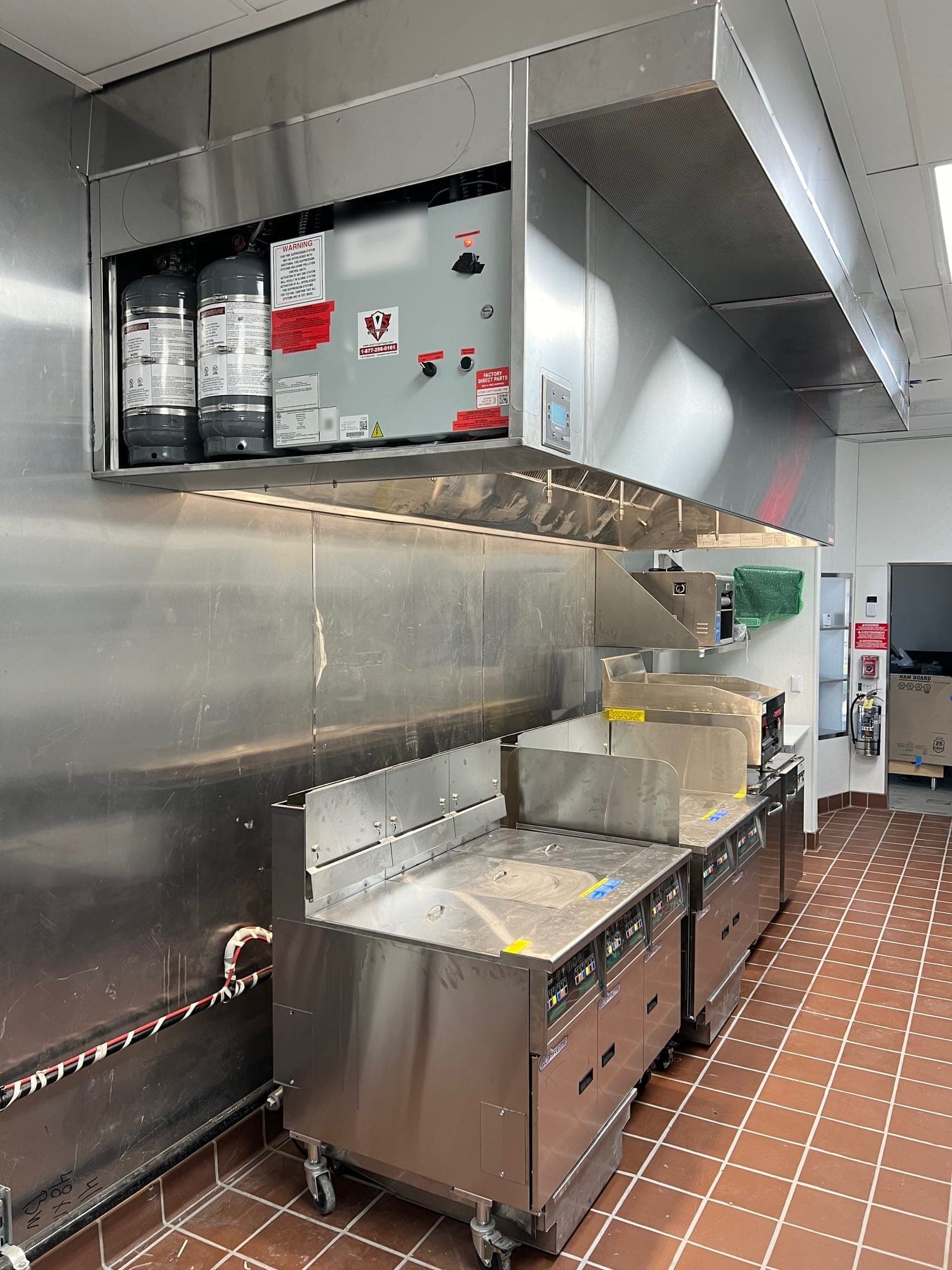Completed CaptiveAire hood with tank cylinders and control panel installed over the fryers