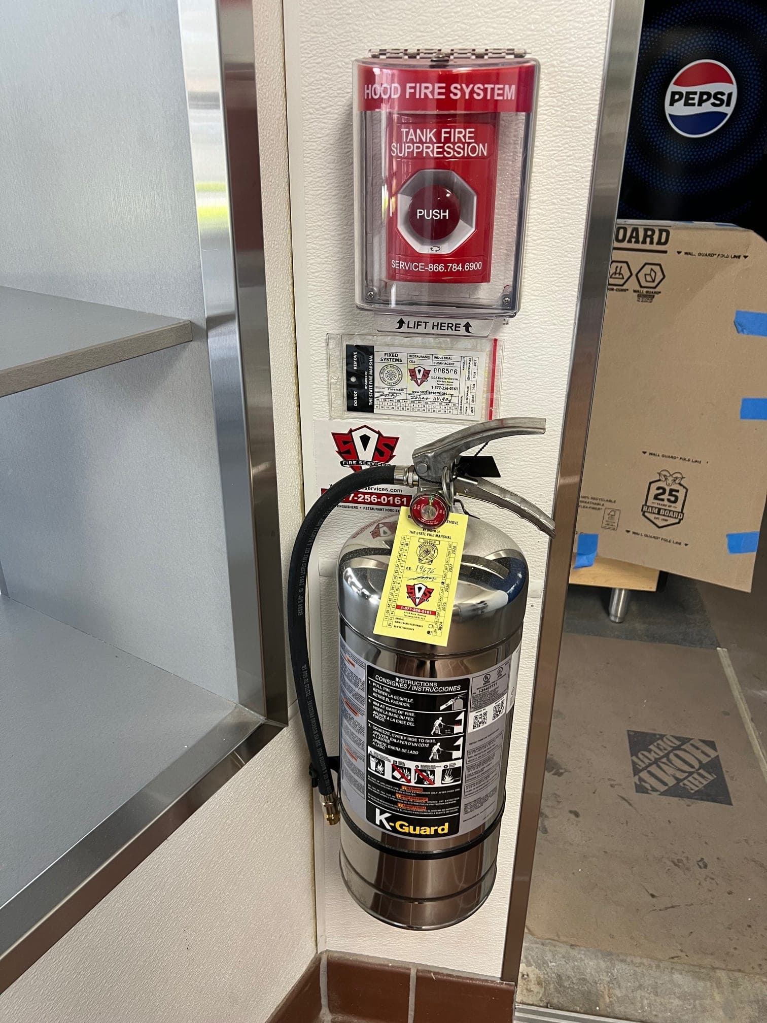 Hood fire system manual push station, service tag and tagged Class K extinguisher on a wall pillar