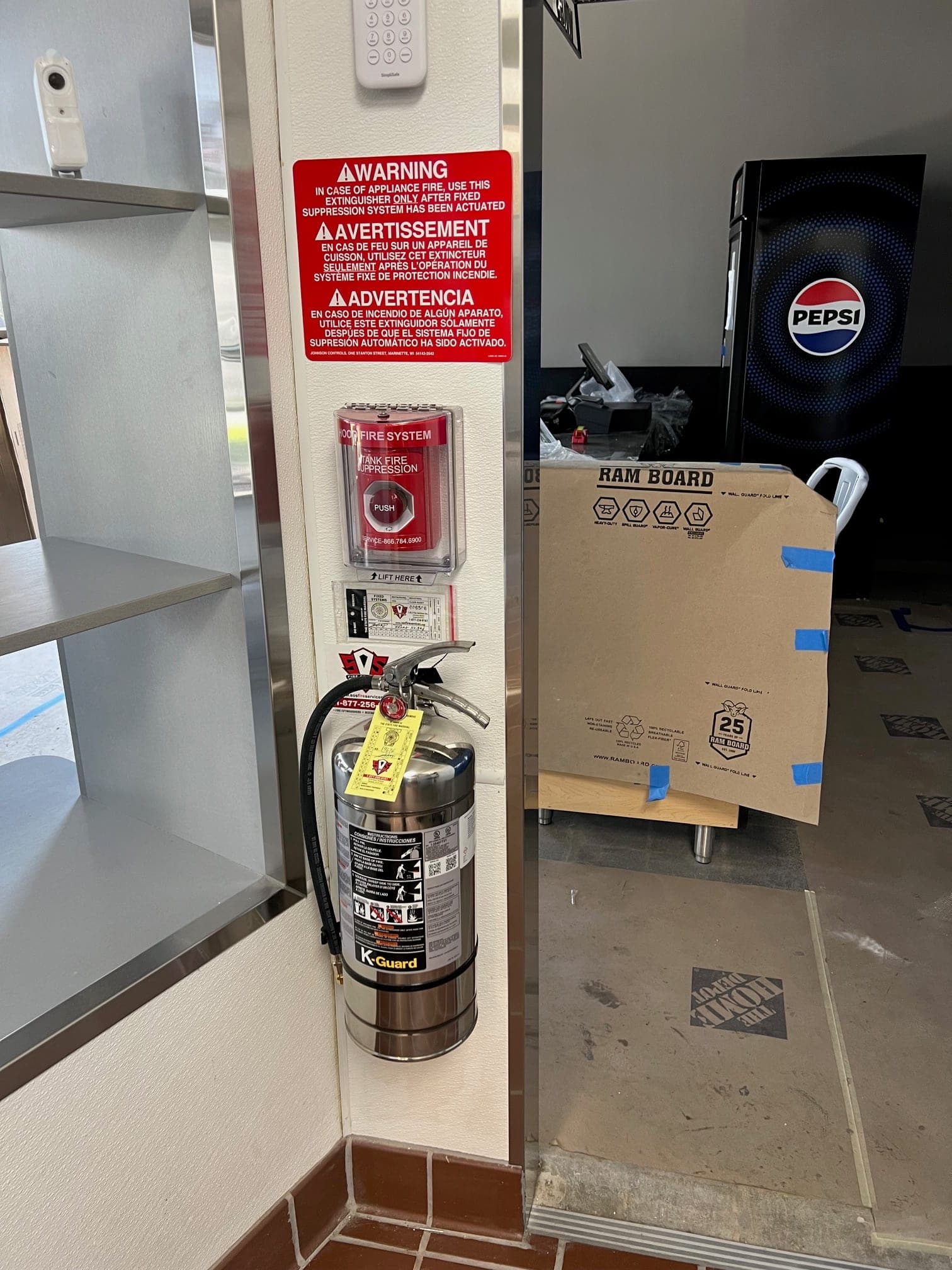 Pillar with a Class K warning sign, manual push station and Class K extinguisher by the kitchen exit