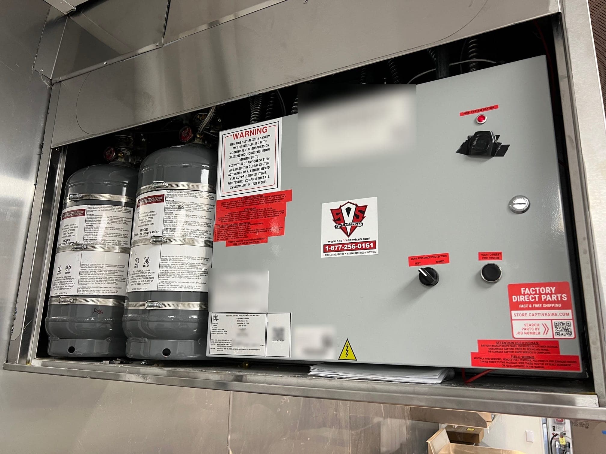 Close view of two CaptiveAire tank cylinders beside the system control panel inside the hood cabinet