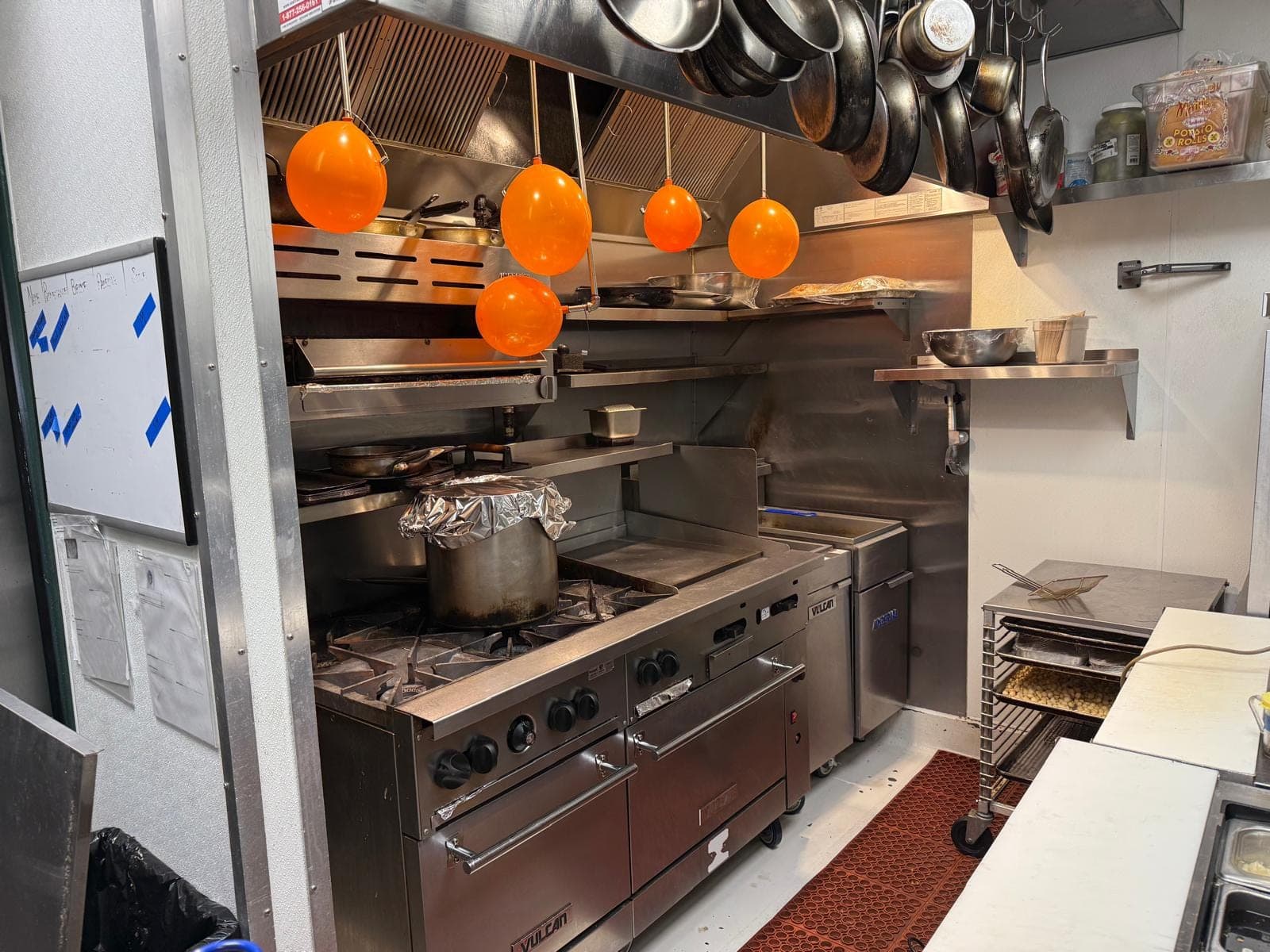 Orange test balloons hanging from every nozzle over a restaurant range and griddle during the semi-annual air test