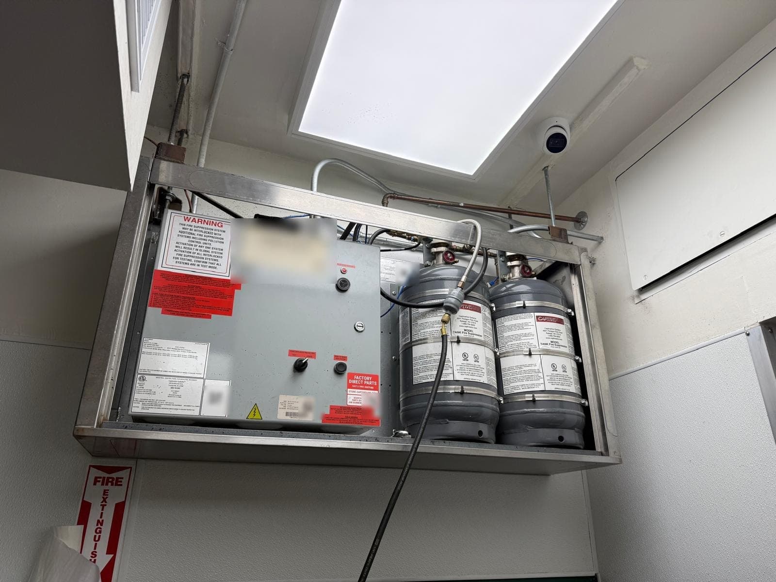 Open CaptiveAire control box beside two agent tanks, with a test air hose connected to the system
