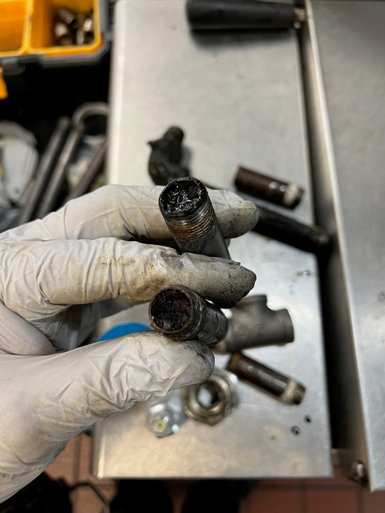 Gloved hands holding two pipe nipples from the suppression system, both openings packed with black grease