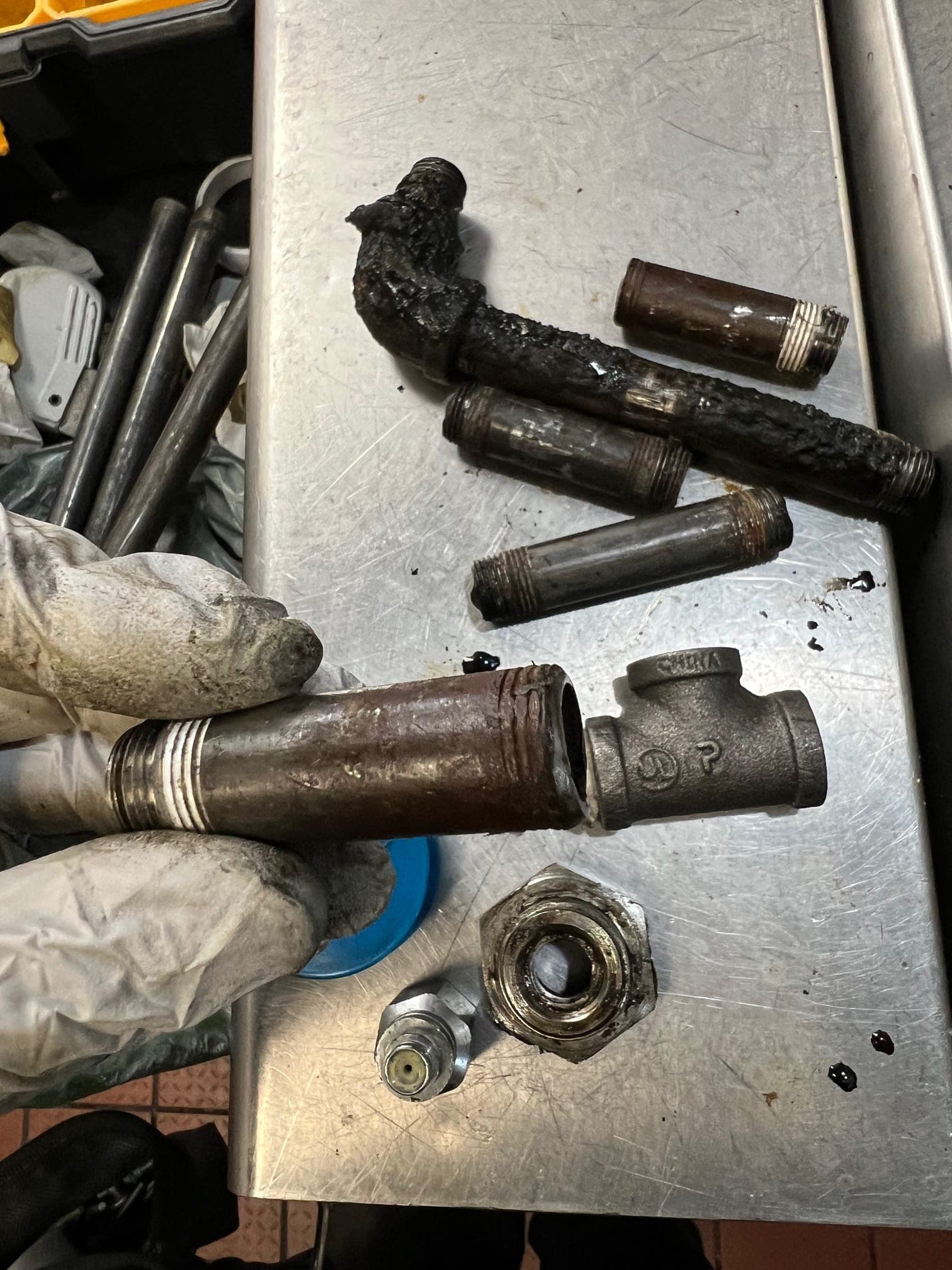 Disassembled suppression piping on a steel table: grease-coated nipples, an elbow and a tee
