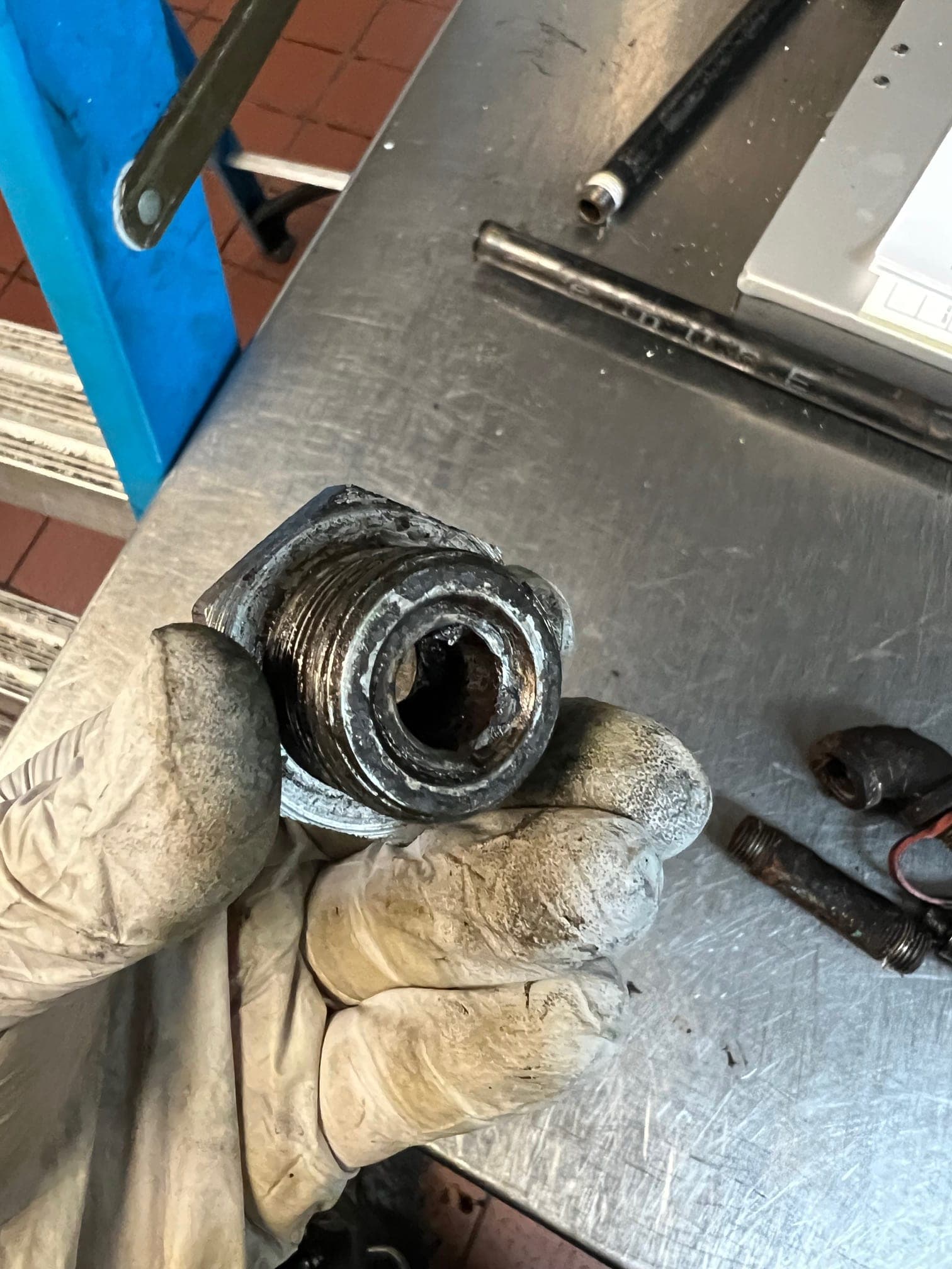 Gloved hand holding a nozzle fitting whose bore is narrowed by grease buildup