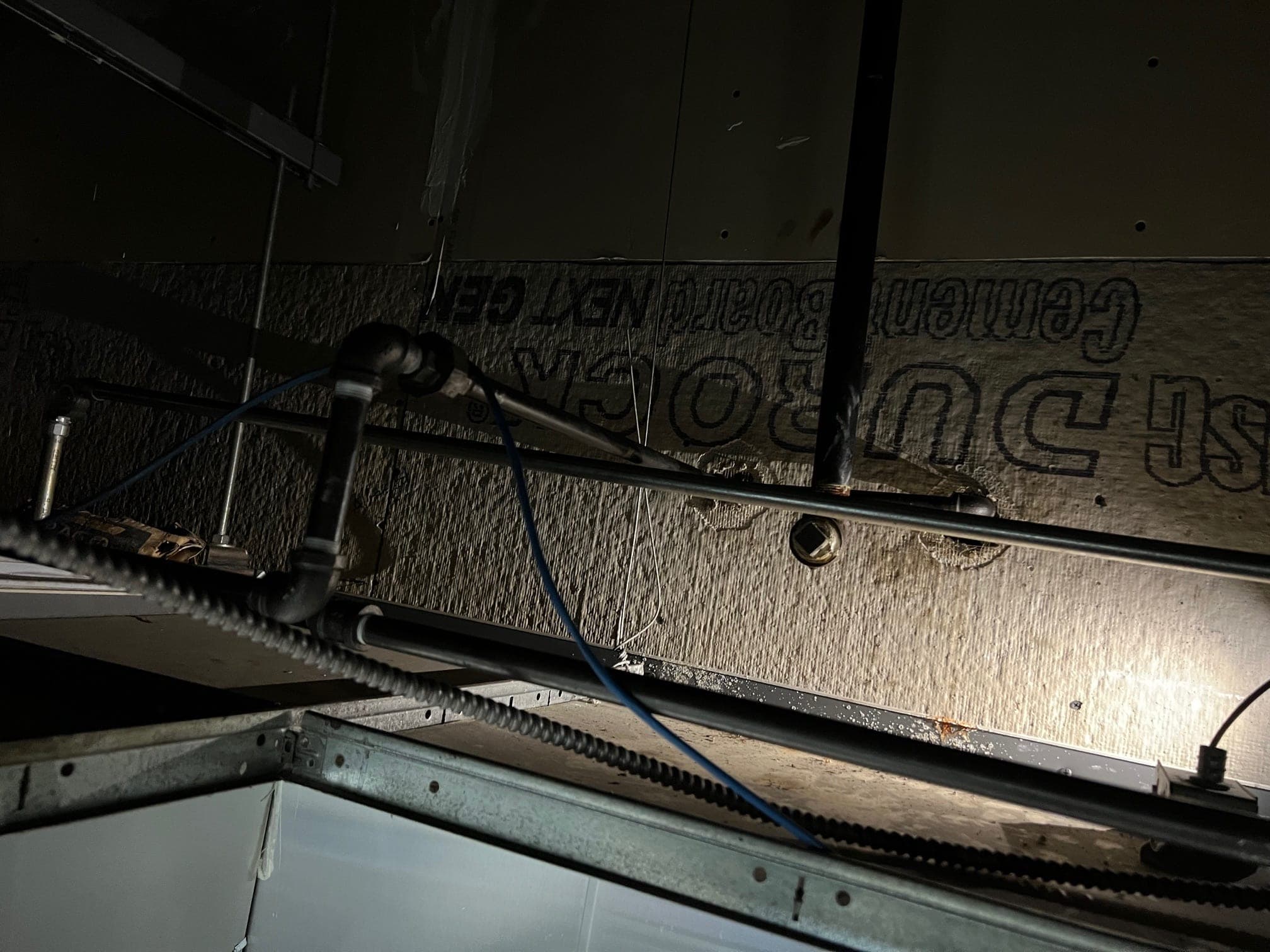 Overhead suppression piping and detection line running above the hood, lit by a flashlight