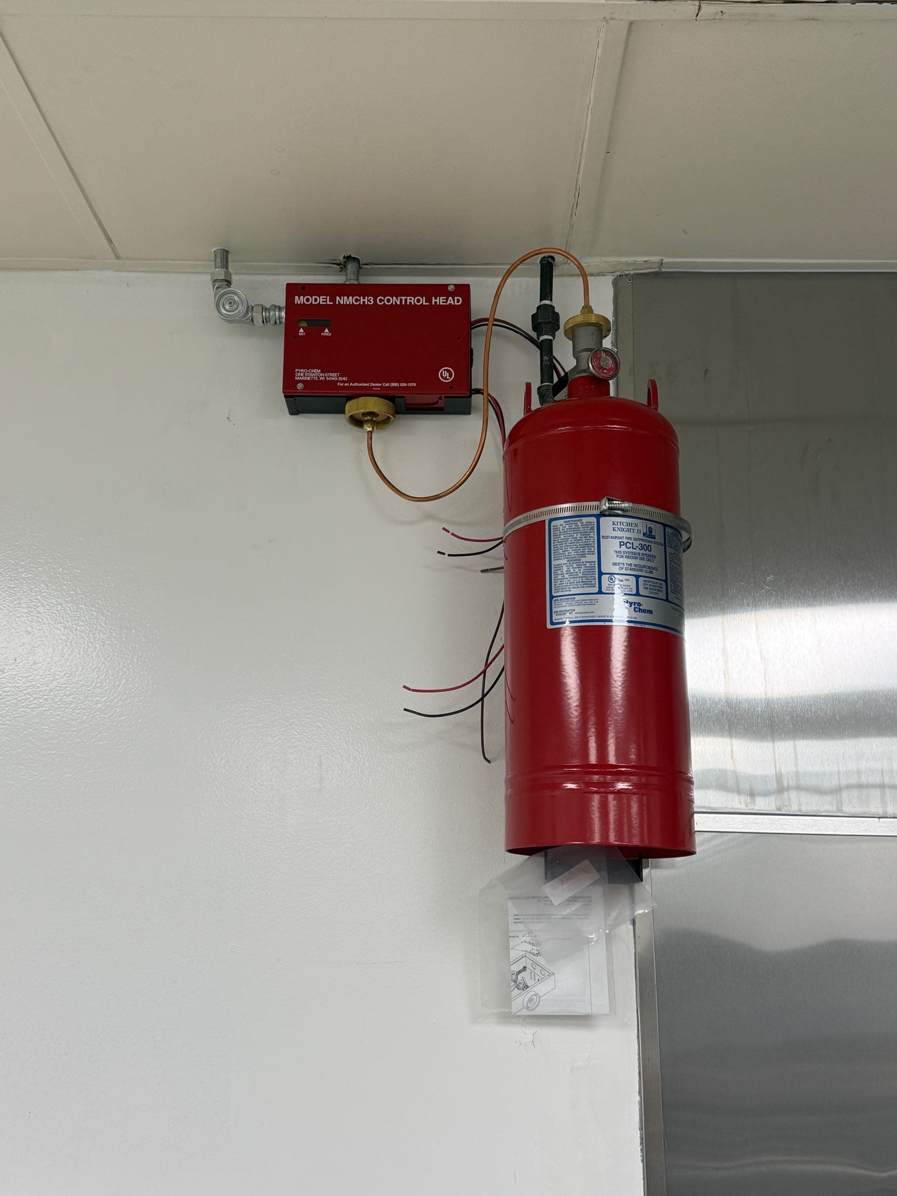 New Pyro-Chem PCL-300 red agent cylinder on a wall bracket below the NMCH3 control head, joined by a copper actuation line