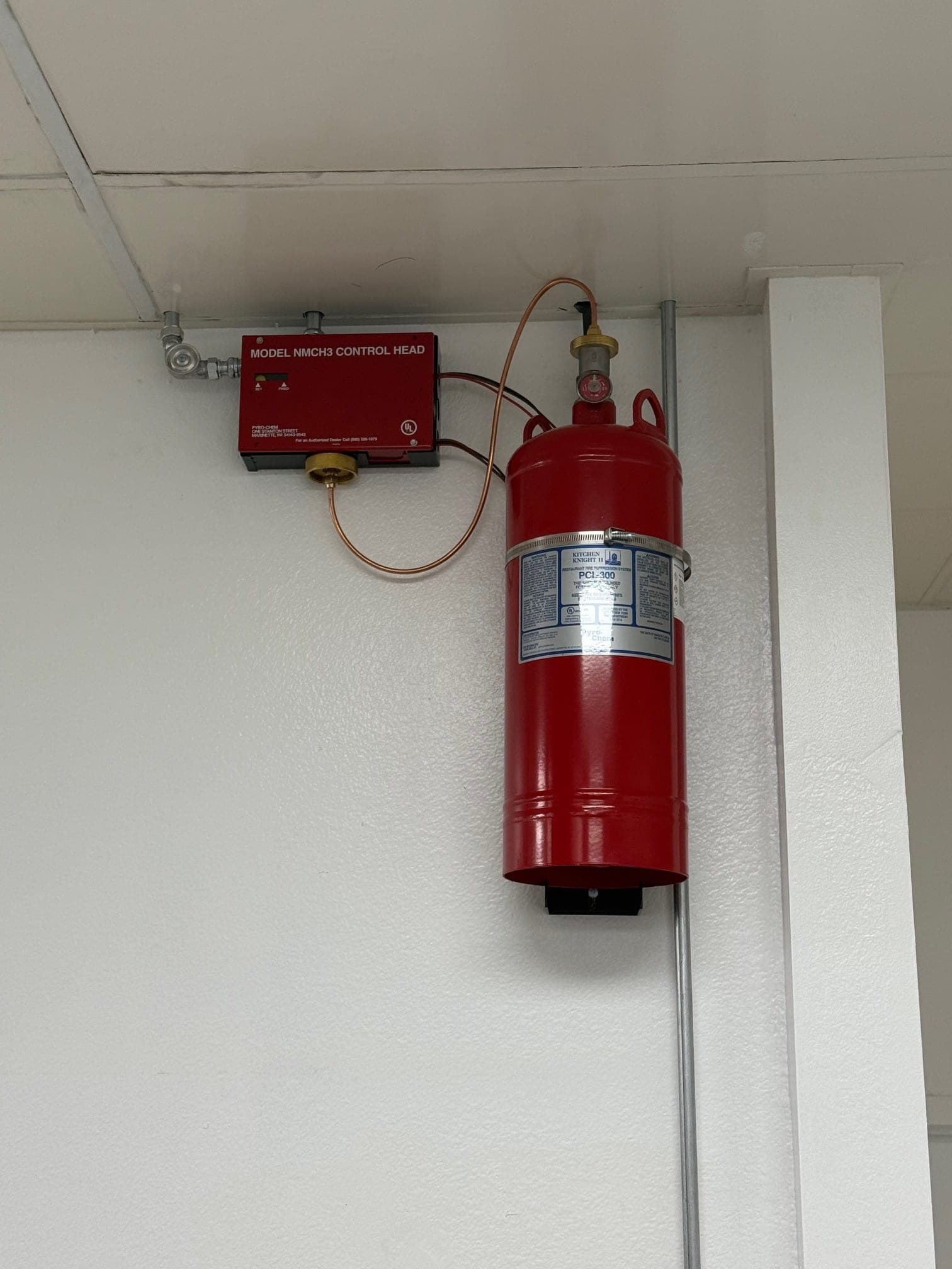 Close view of the NMCH3 control head and PCL-300 cylinder, with conduit running down the wall