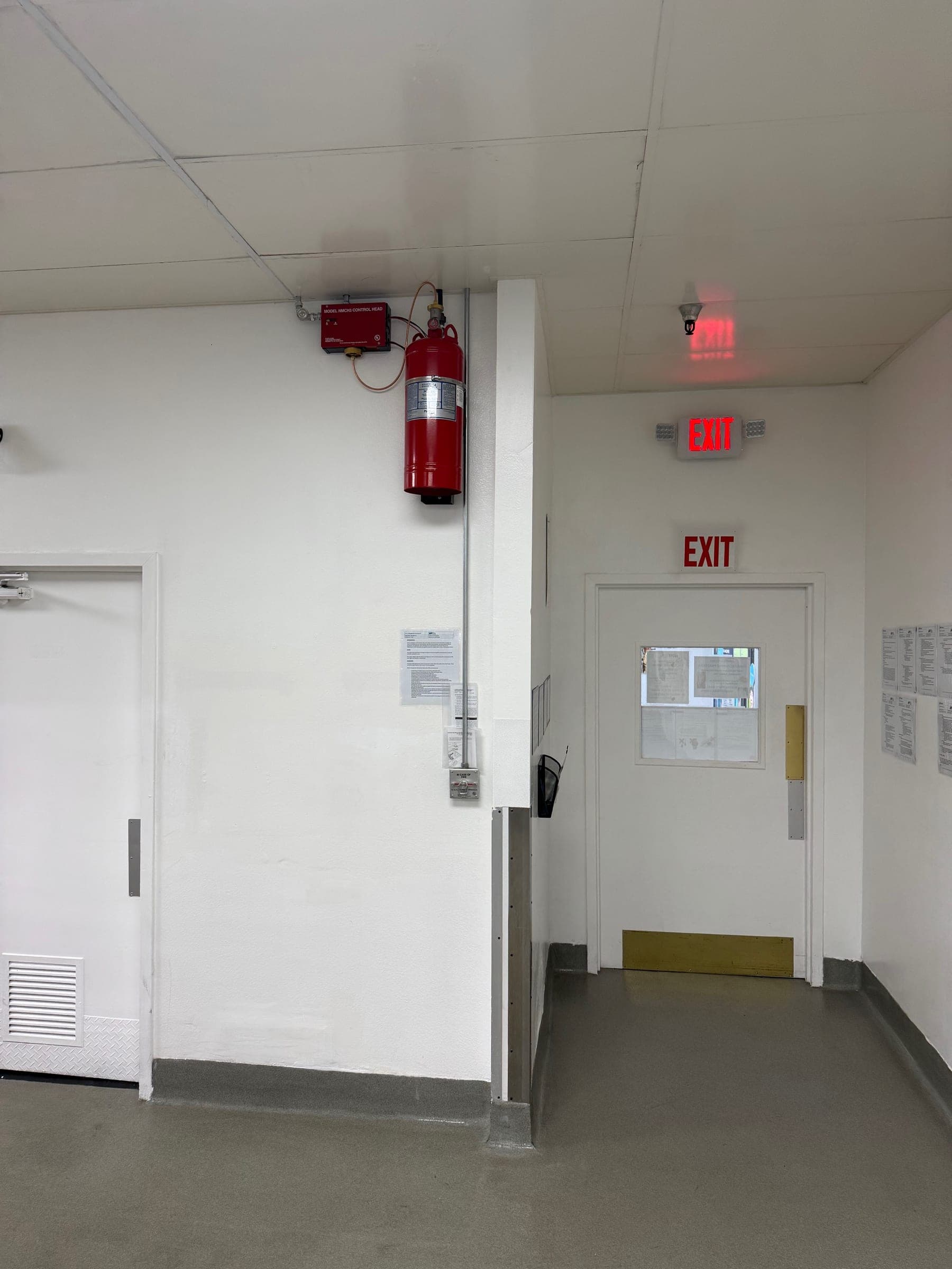 Pyro-Chem cylinder and control head high on a wall next to the kitchen exit, with conduit to the pull station