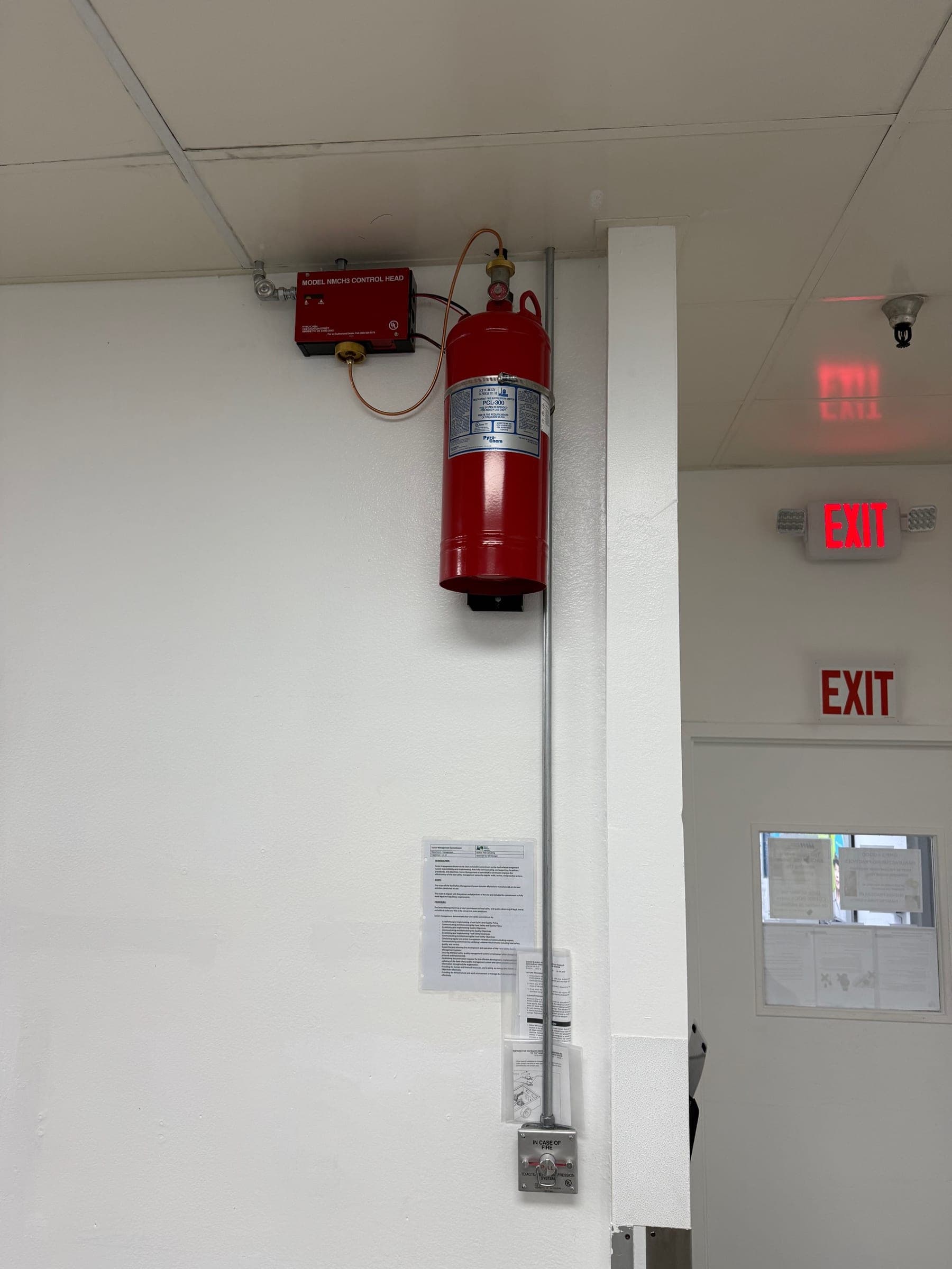 Conduit running down the wall from the Pyro-Chem control head to a manual pull station beside the exit door