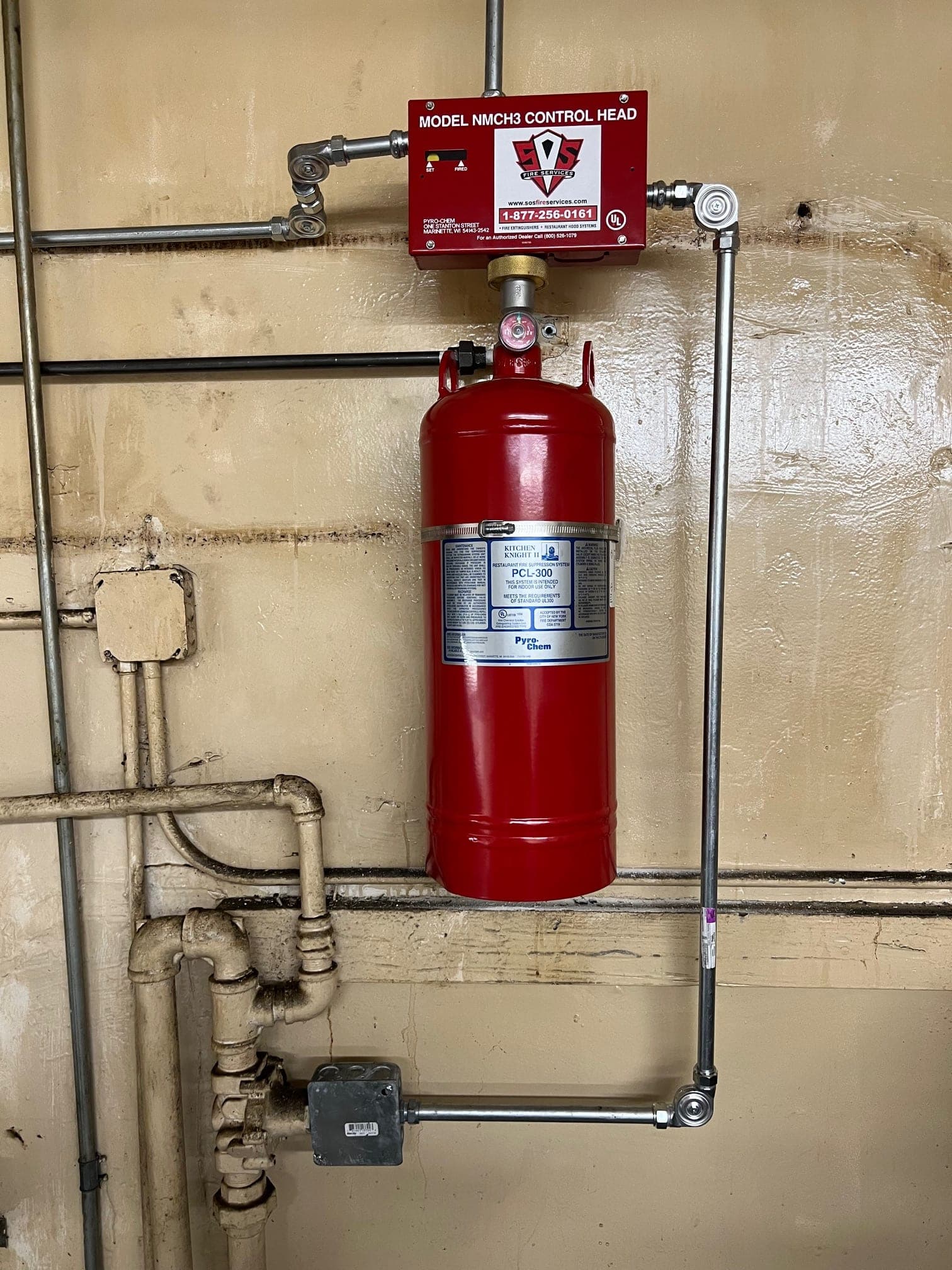 Red Pyro-Chem PCL-300 cylinder under its NMCH3 control head, mounted on a kitchen wall with conduit and the gas line