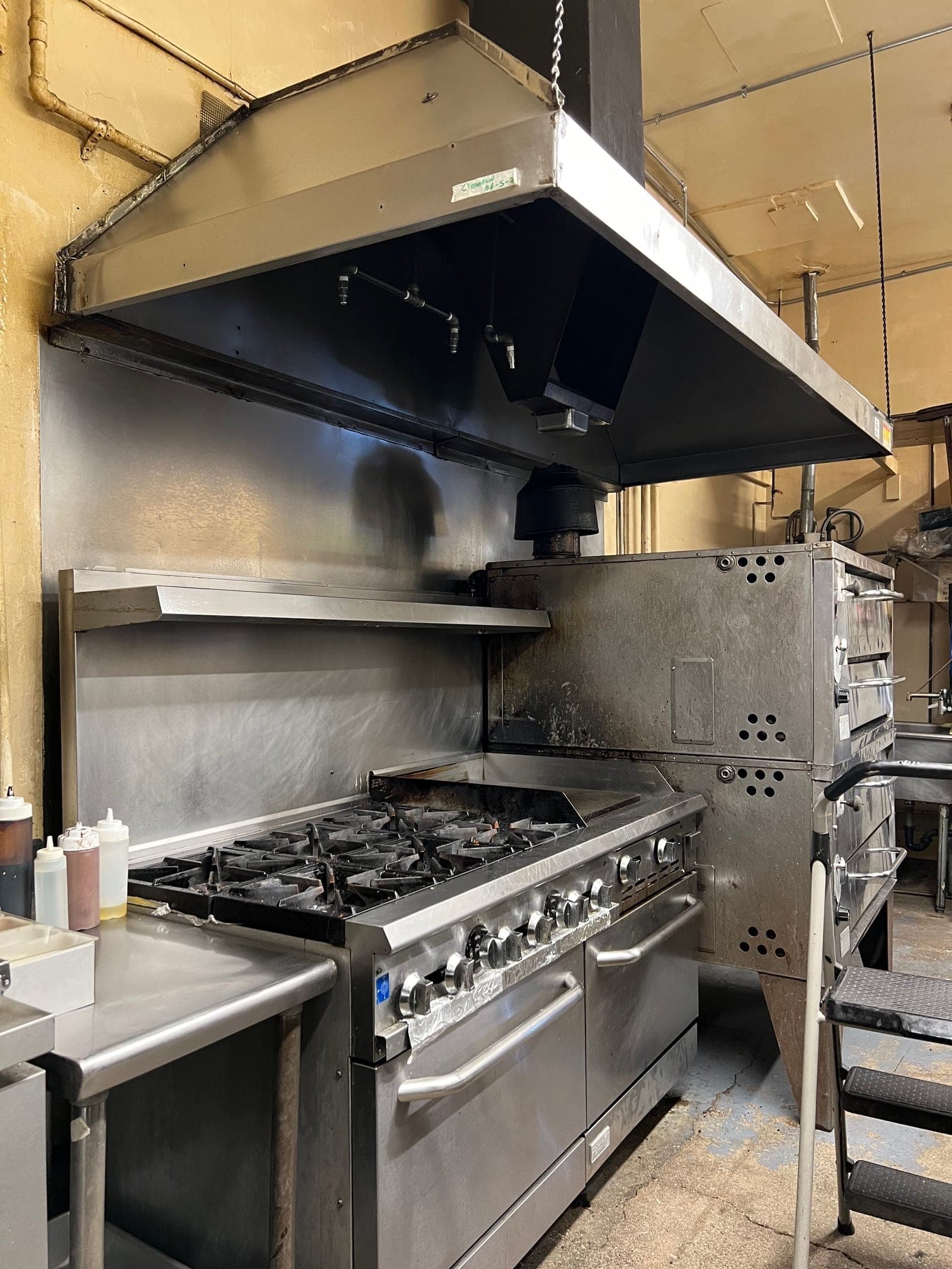 Kitchen cooking line with a range and pizza ovens under the stainless exhaust hood