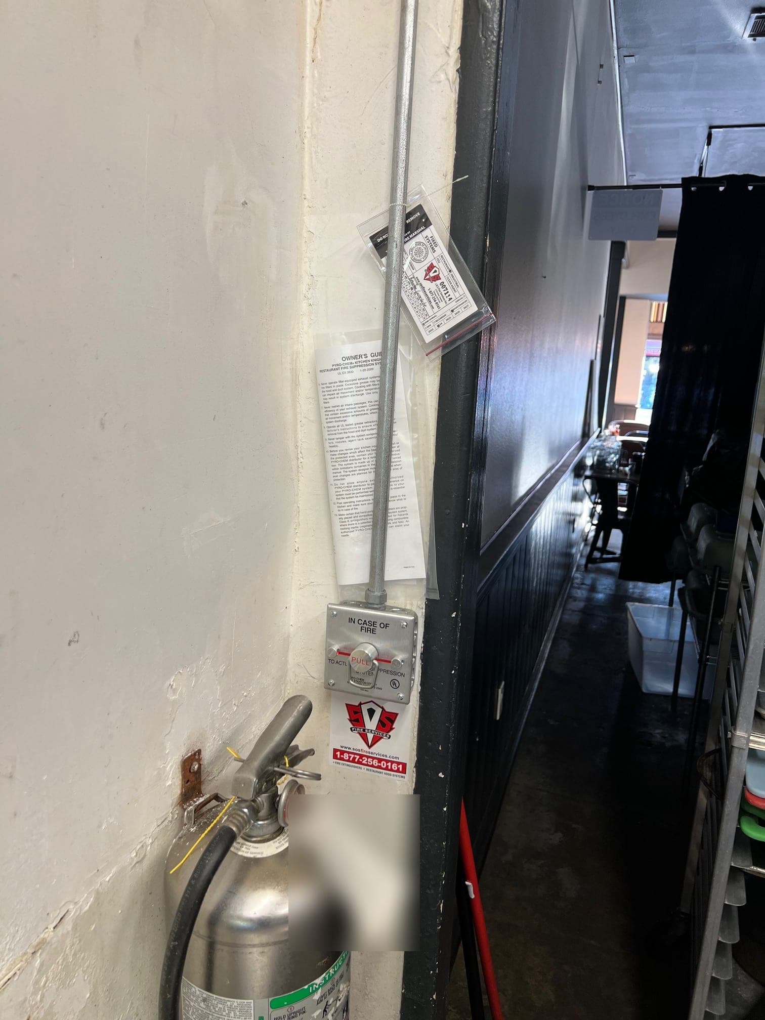 Manual pull station with a service tag on its conduit, above a Class K wet chemical extinguisher