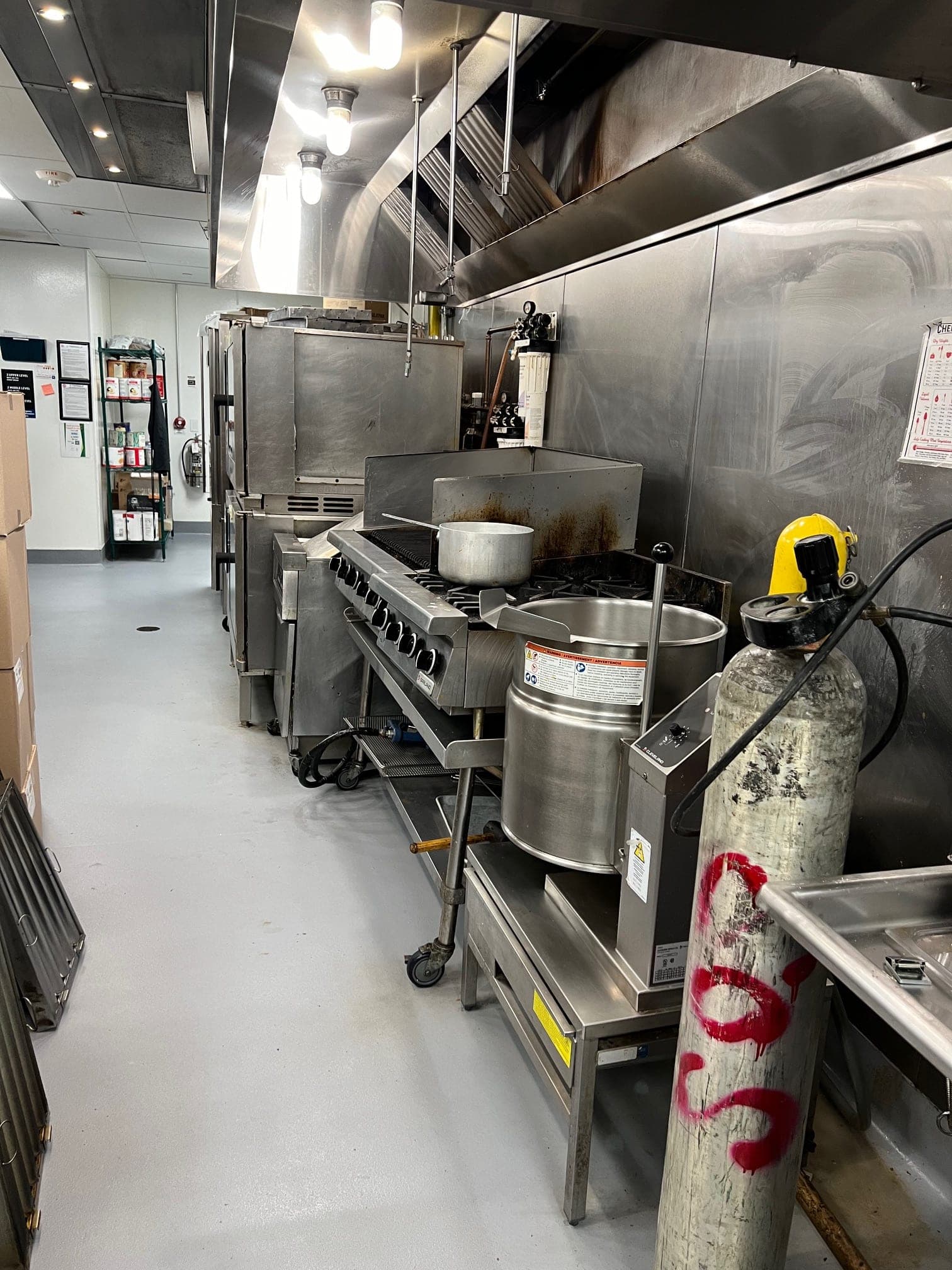 Long commercial kitchen line with ranges and kettles under exhaust hoods