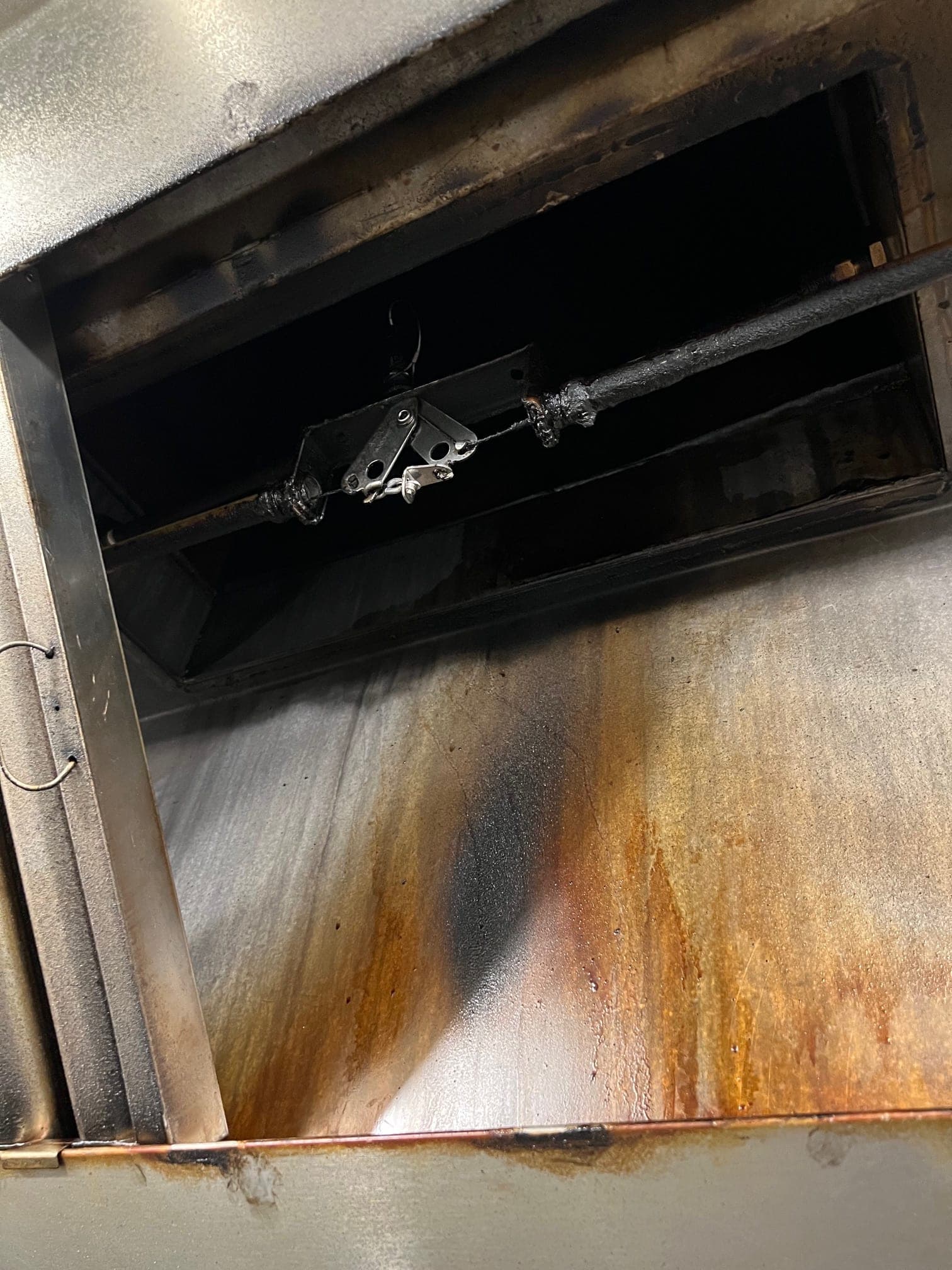 Fusible link bracket on the detection line inside a hood, the hood wall streaked with grease