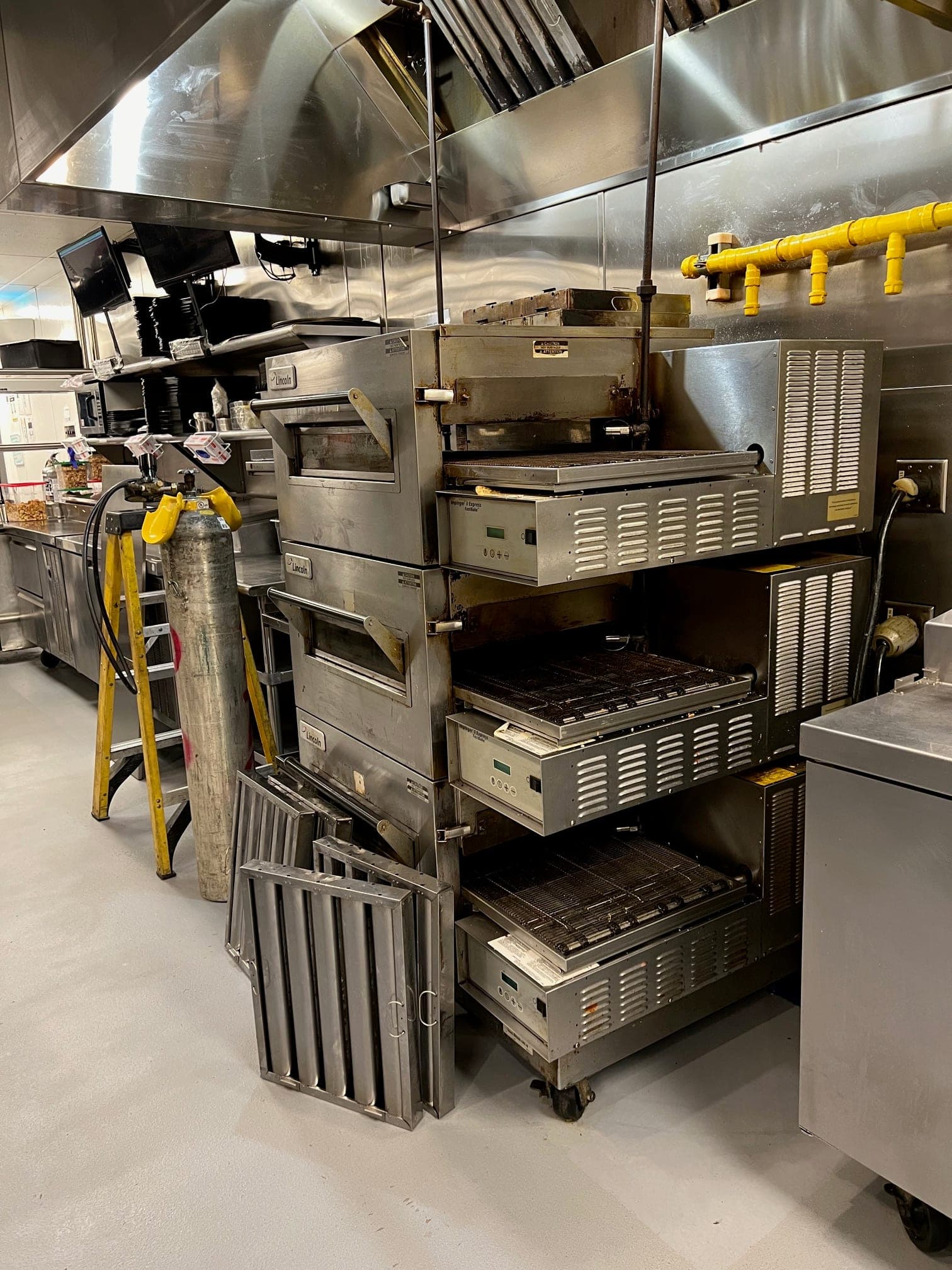 Stacked conveyor ovens under a stainless exhaust hood in a large commercial kitchen
