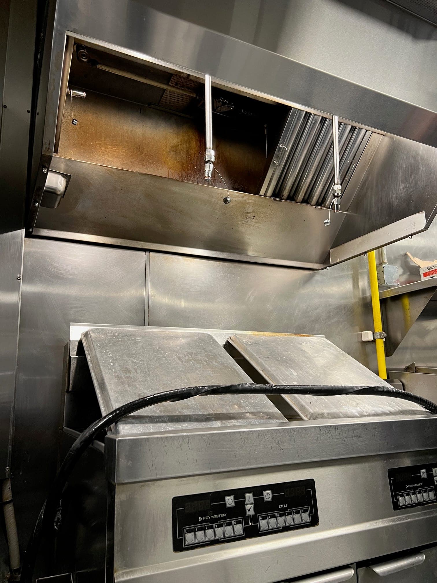 Suppression nozzle drops aimed over a fryer under the exhaust hood