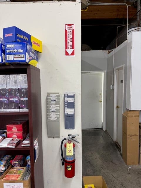 ABC extinguisher hung beside a shelving unit with an arrow sign above marking its spot in the warehouse