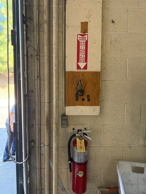 Tagged ABC extinguisher mounted on a block wall beside a roll-up door, with location sign above