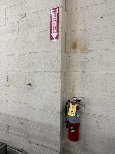 ABC extinguisher on a painted block wall with its bilingual location sign mounted on the adjacent wall