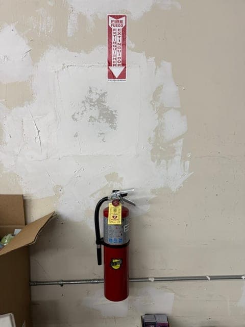 ABC extinguisher hung on a freshly patched wall with a bilingual location sign centered above it