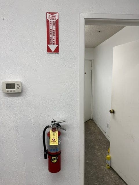 Tagged ABC extinguisher mounted beside a hallway doorway with a location sign above it