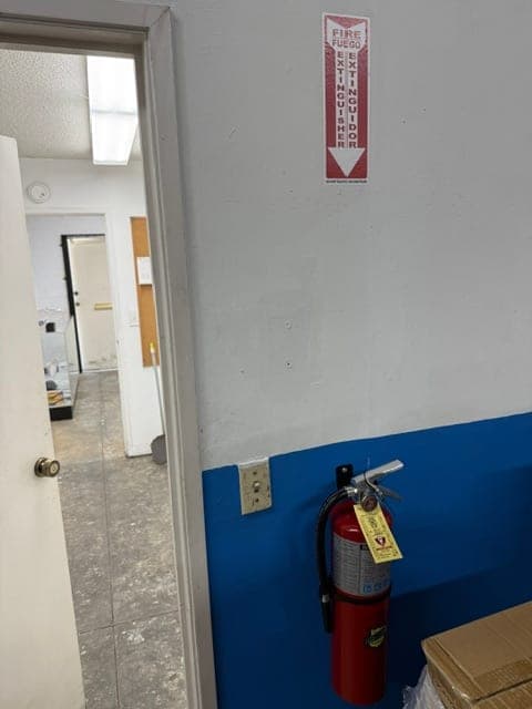 ABC extinguisher mounted on a two-tone wall beside a doorway, location sign high on the wall