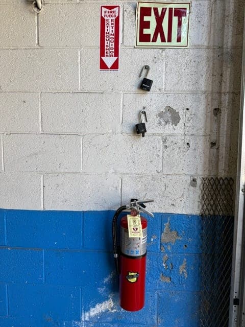 Tagged ABC extinguisher on a blue and white block wall, with location sign beside an exit sign